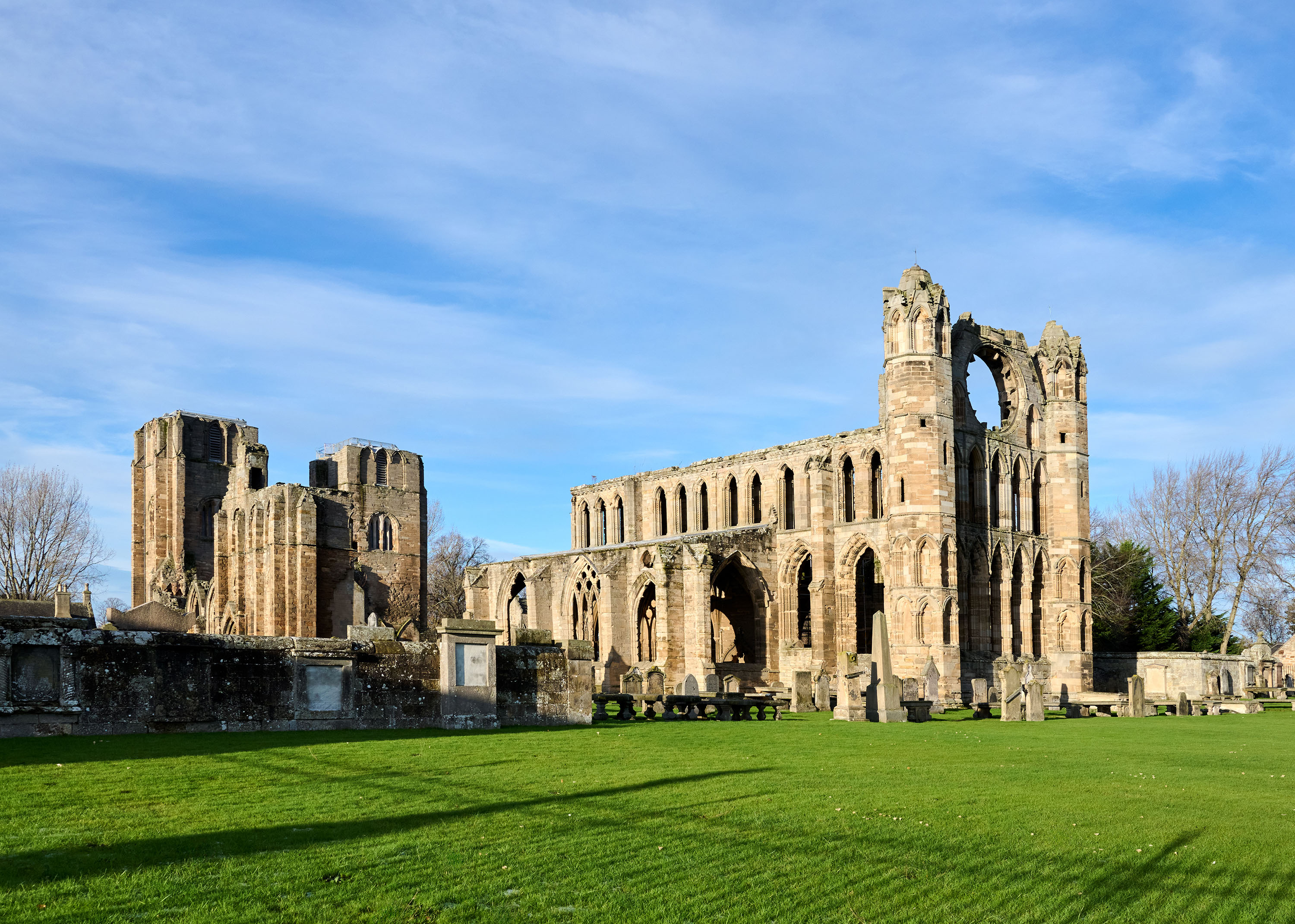 Ruins of a beautiful cathedral and its impressive rose window basking under blue skies and a lush green lawn