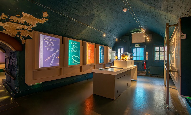 A room with a curved ceiling, where the walls are covered in exhibition text. In the middle of the room, there is a cabinet filled with reconstructed heads of people from medieval times.