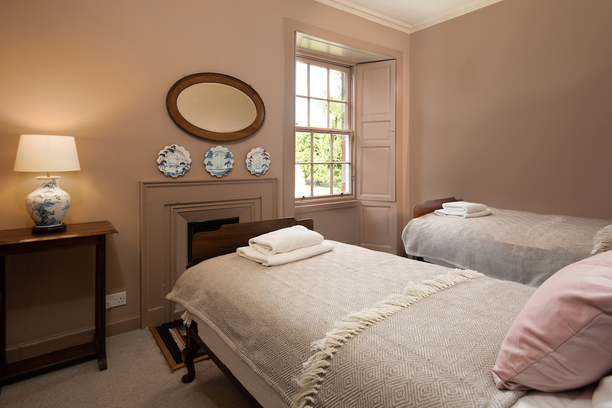 A pink twin bedroom, with blue and white plates and a lamp, a dark wooden mirror and soft pink and grey bedding 
