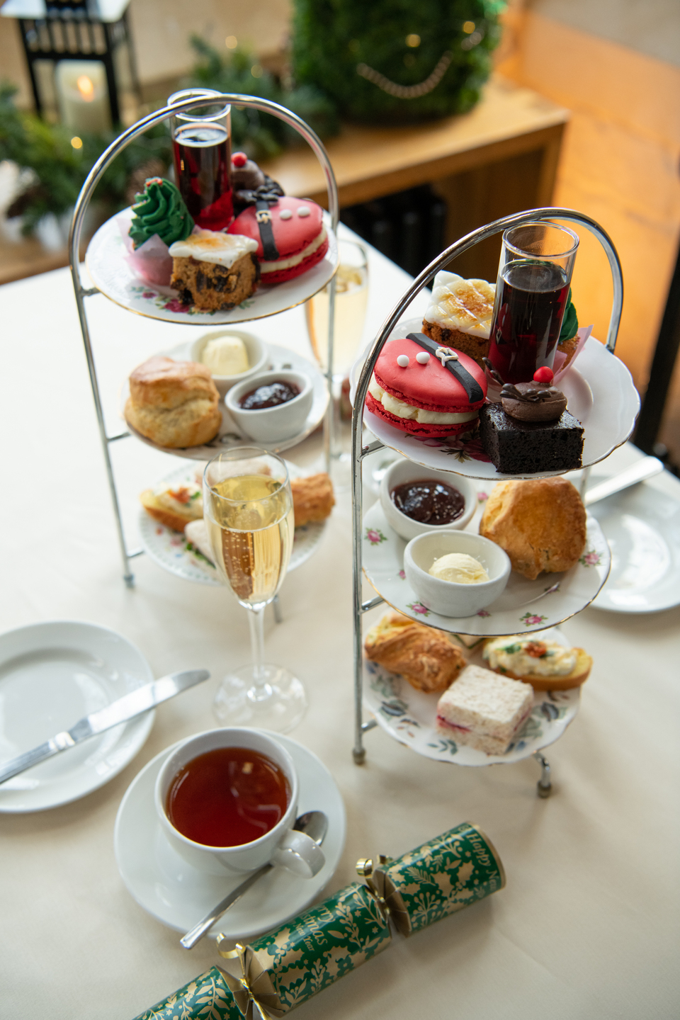 Two cake stands with three layers, there is an afternoon tea (sandwiches and cakes) on the stand. There are plates and a tea on the table, as well as a Christmas cracker. 