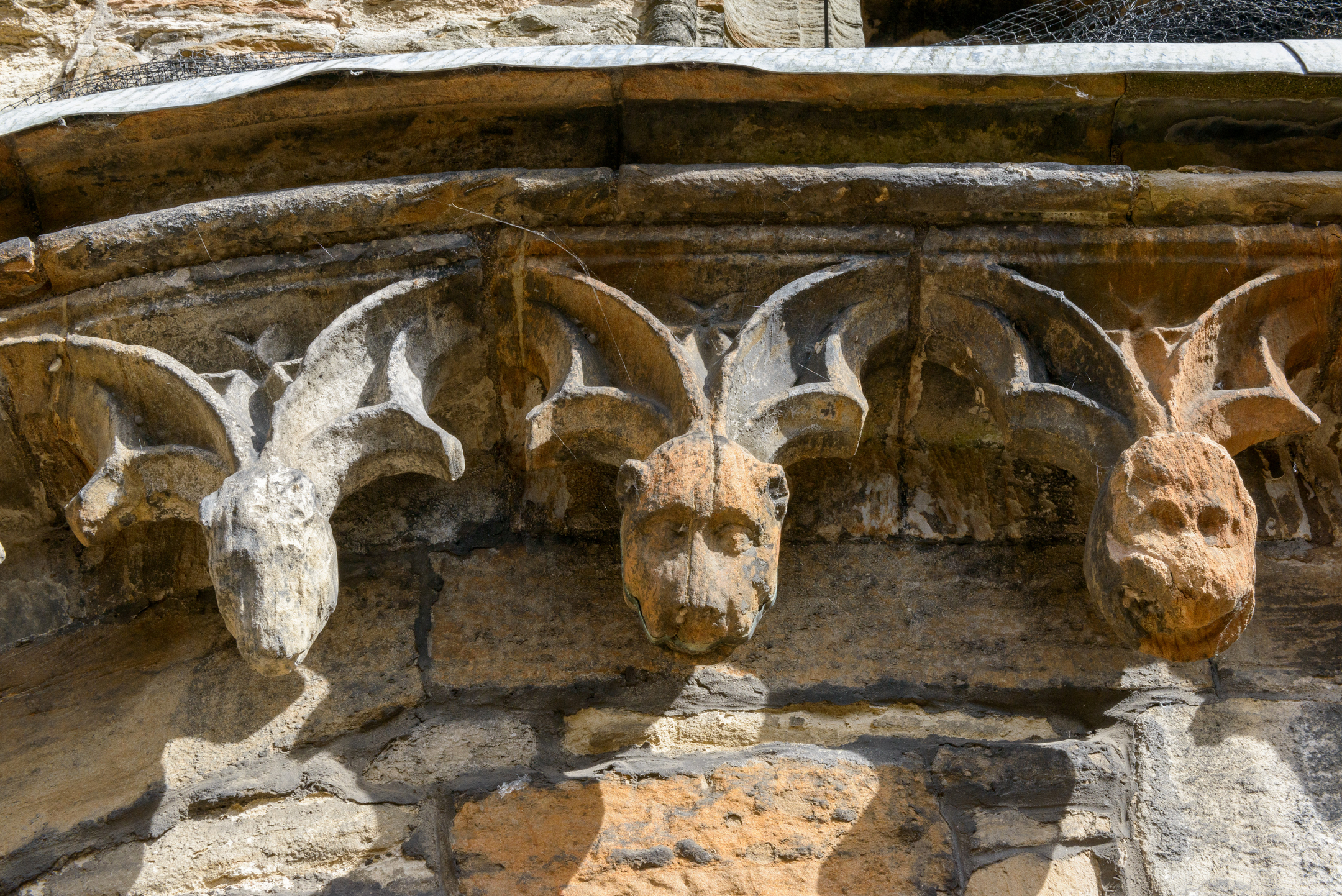 Carved features on a stone wall show animal heads hanging down from decorative curves