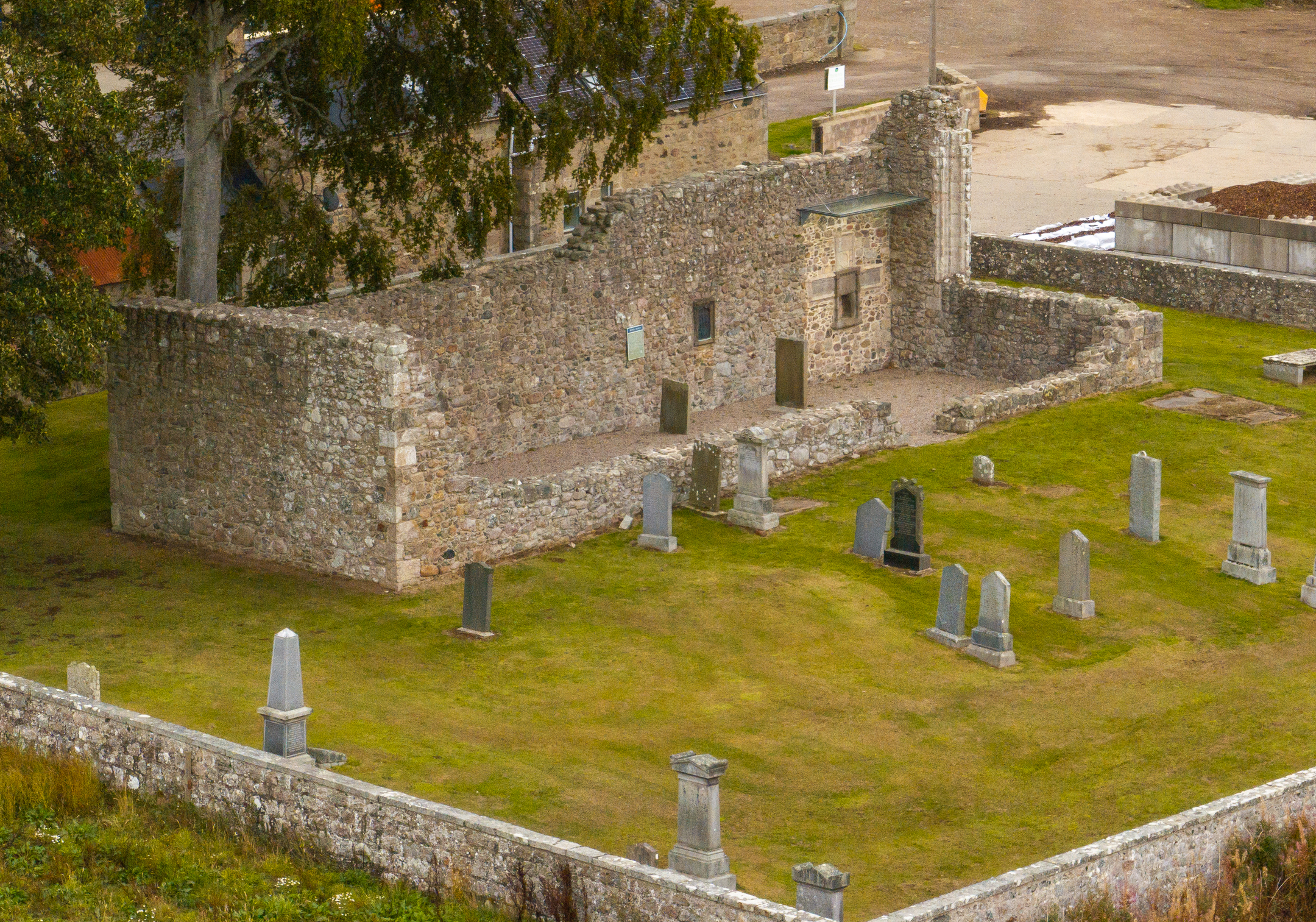Aerial view of Kinkell Church ruins and surrounding graveyard within a rectangular stone boundary.