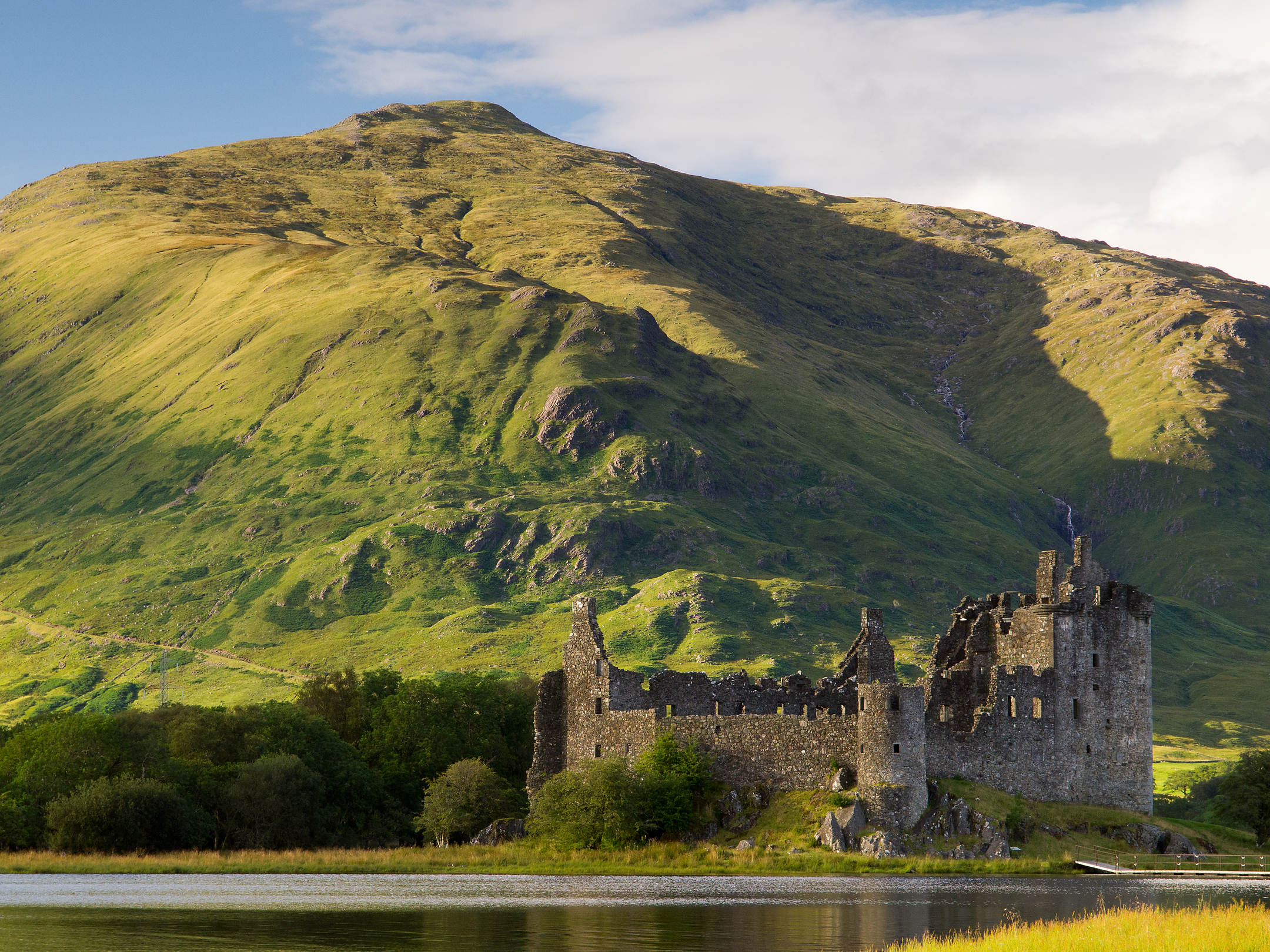 Castle in front of a mountain with a loch in the foreground