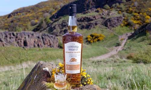'Defender of the Nation' Whisky bottle and glass sitting on a rock with a background view of Arthur's Seat