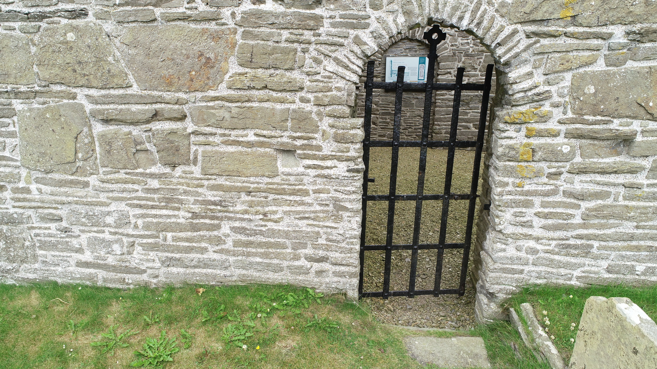Black metal gate set within a small arched doorway in the church’s stone exterior wall