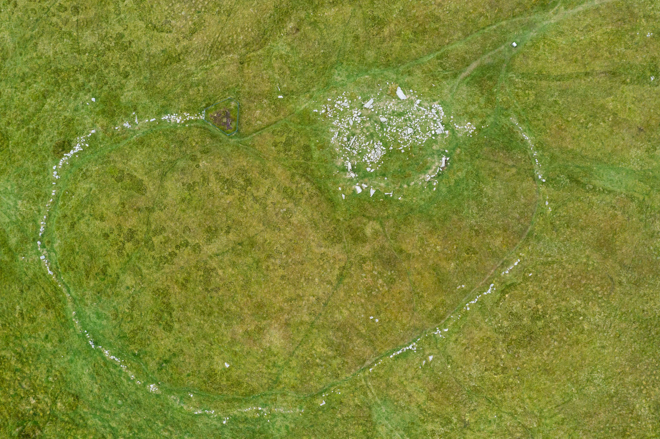 Aerial view showing circular cairn and surrounding stone ring on green moorland.
