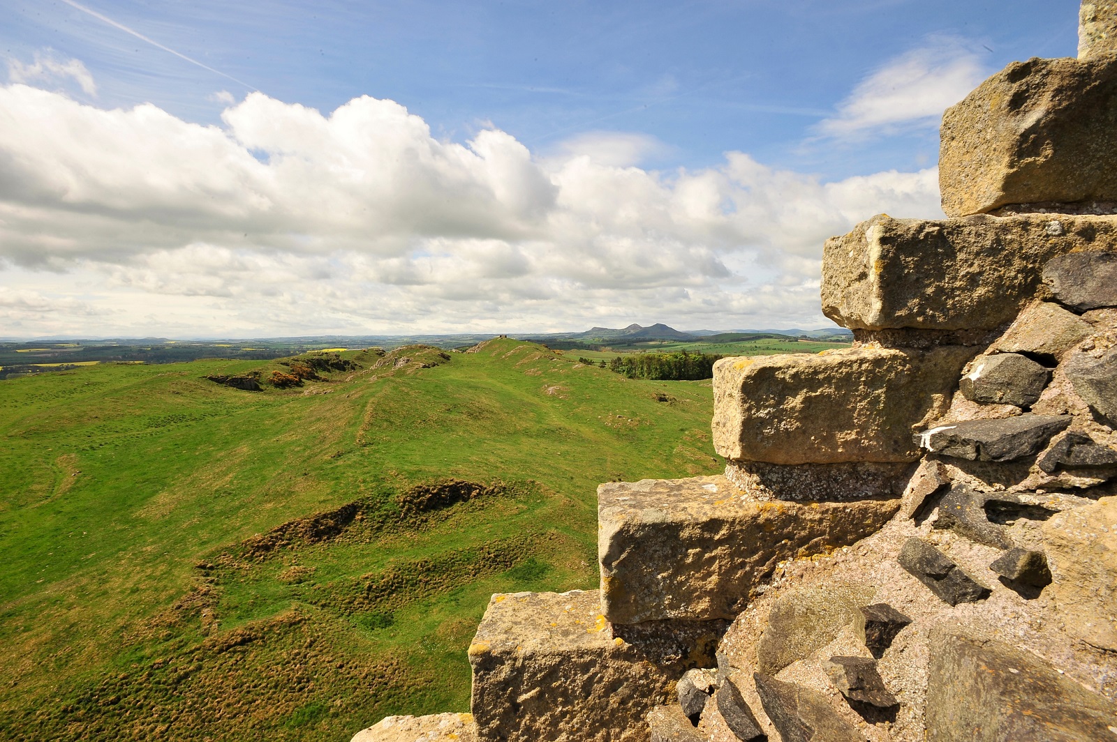 View from stone ruins looking out across rolling green hills beneath a cloudy sky.