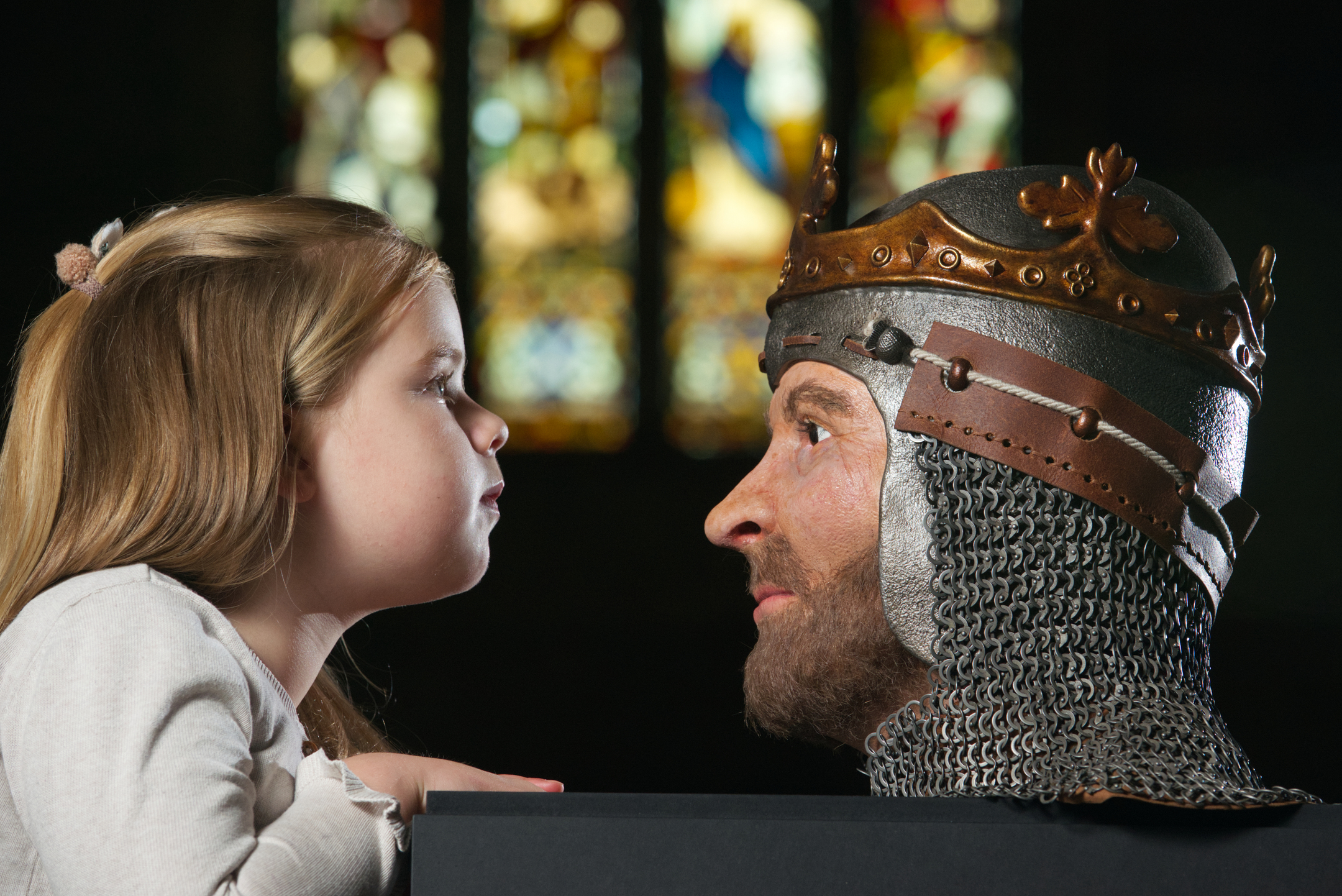 A child leans over a display stand to look at a 3D reconstruction of Robert the Bruce's head, which is adorned with a crown and chainmail.