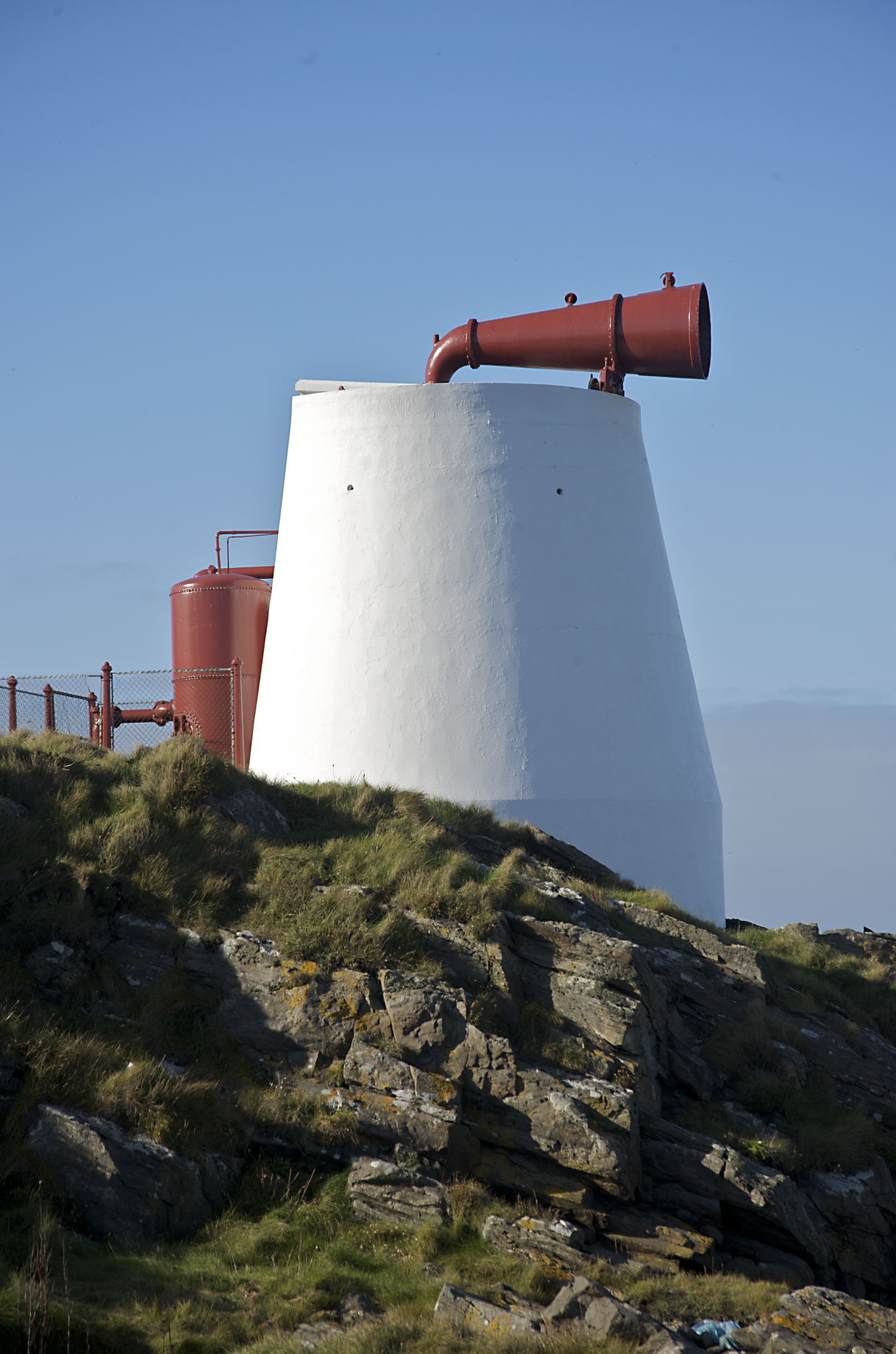 A bright red foghorn positioned atop a white base. 