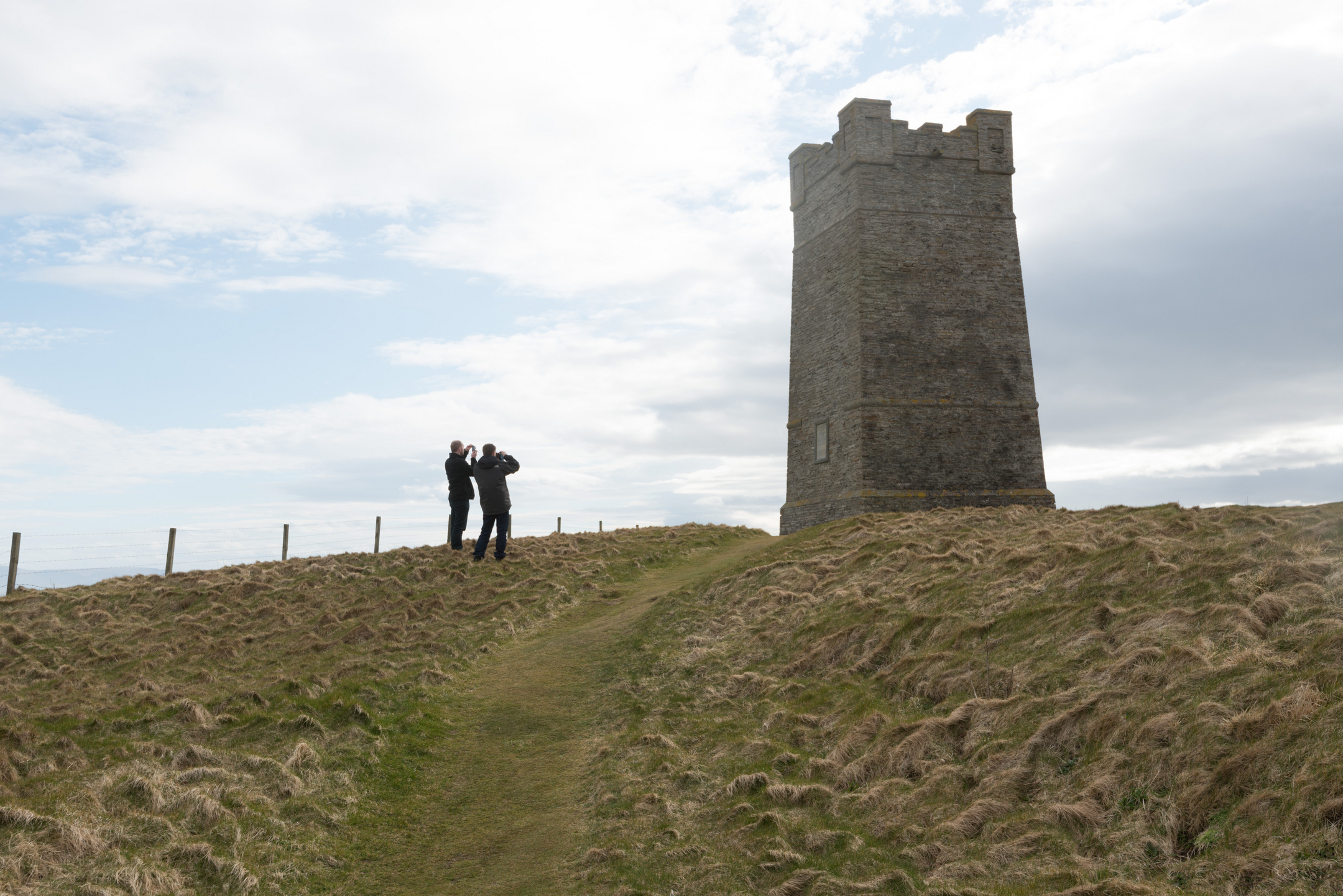 HES employees photograph a large, square stone tower in an isolated setting. 