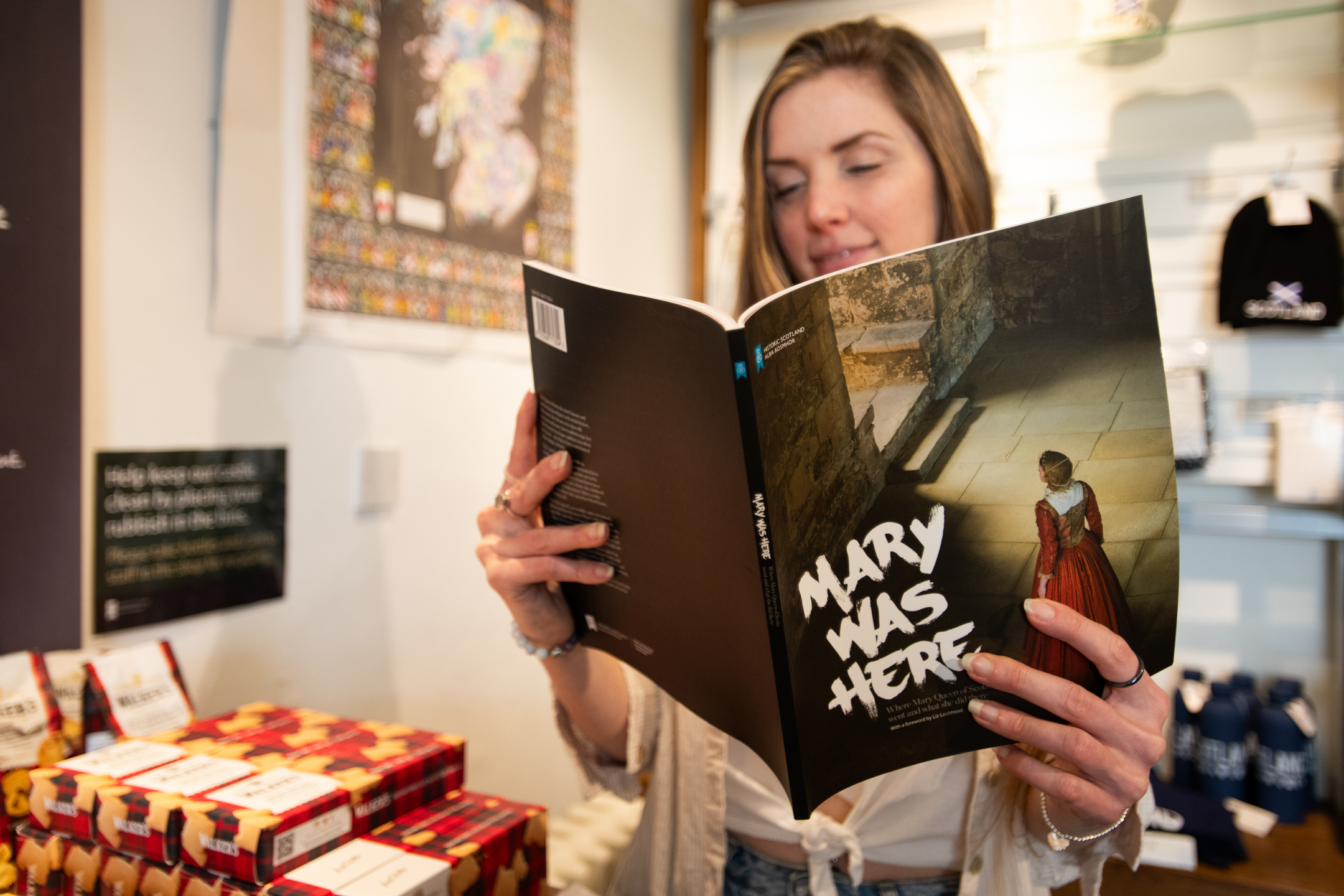 A person stands inside a gift shop reading a book titled “Mary Was Here”, with shelves of merchandise behind them.