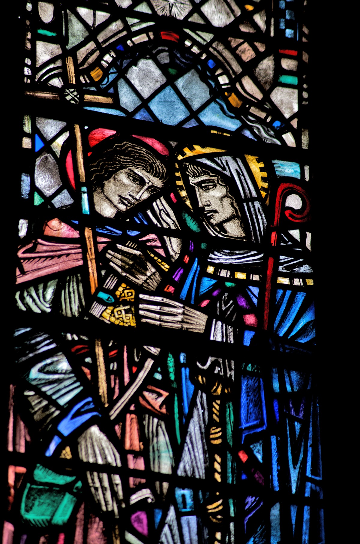 Stained‑glass window featuring two haloed religious figures in detailed robes, surrounded by intricate geometric and symbolic patterns.