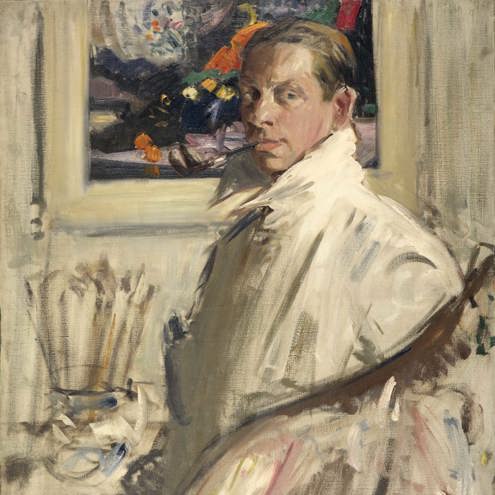 Portrait oil painting of an artist in his studio. Next to him stands a large jug filled with paint brushes, and behind is a colourful painting hanging on the wall.