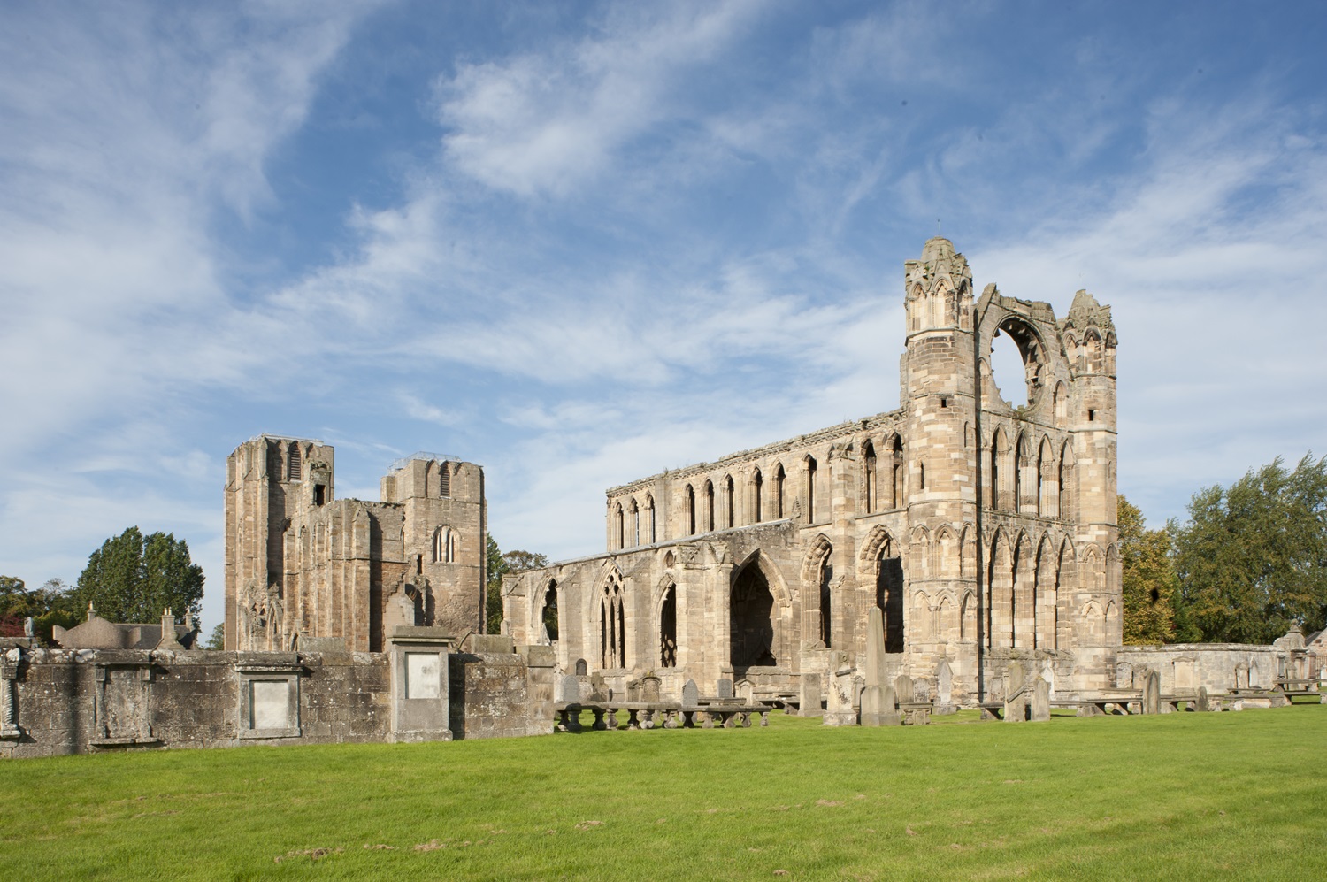 A large, worn cathedral on a sunny day, with trees in the background. 
