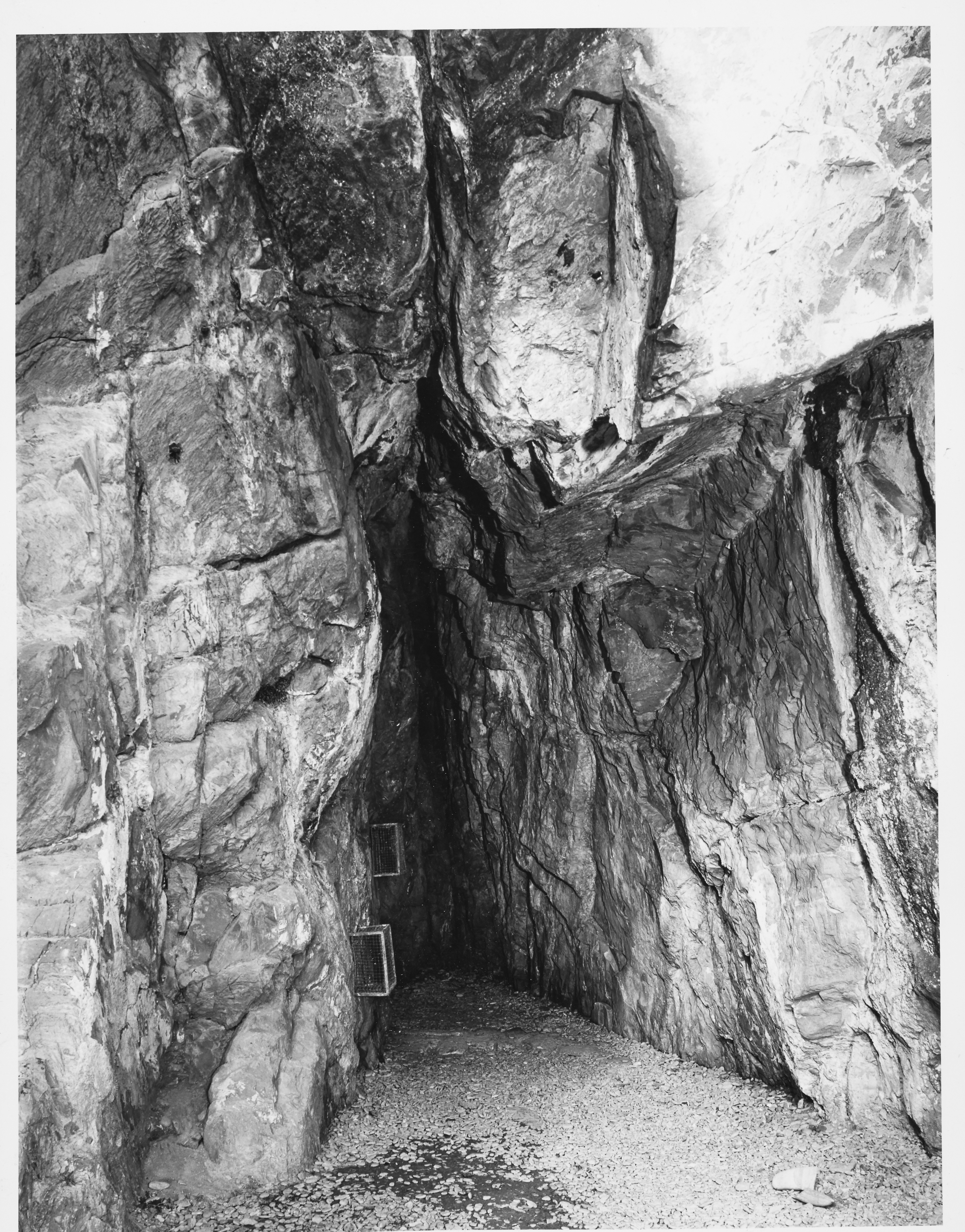 Entrance of a cave between two large, uneven rocks. 