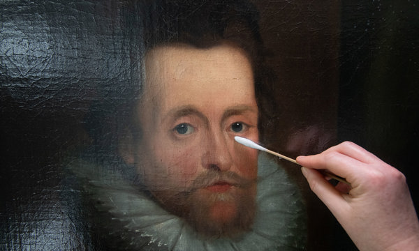 A closeup of an oil painting being gently cleaned with a q-tip.