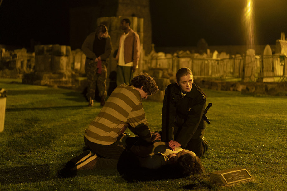 A police officer and a plain clothed person in a graveyard trying to resuscitate a person