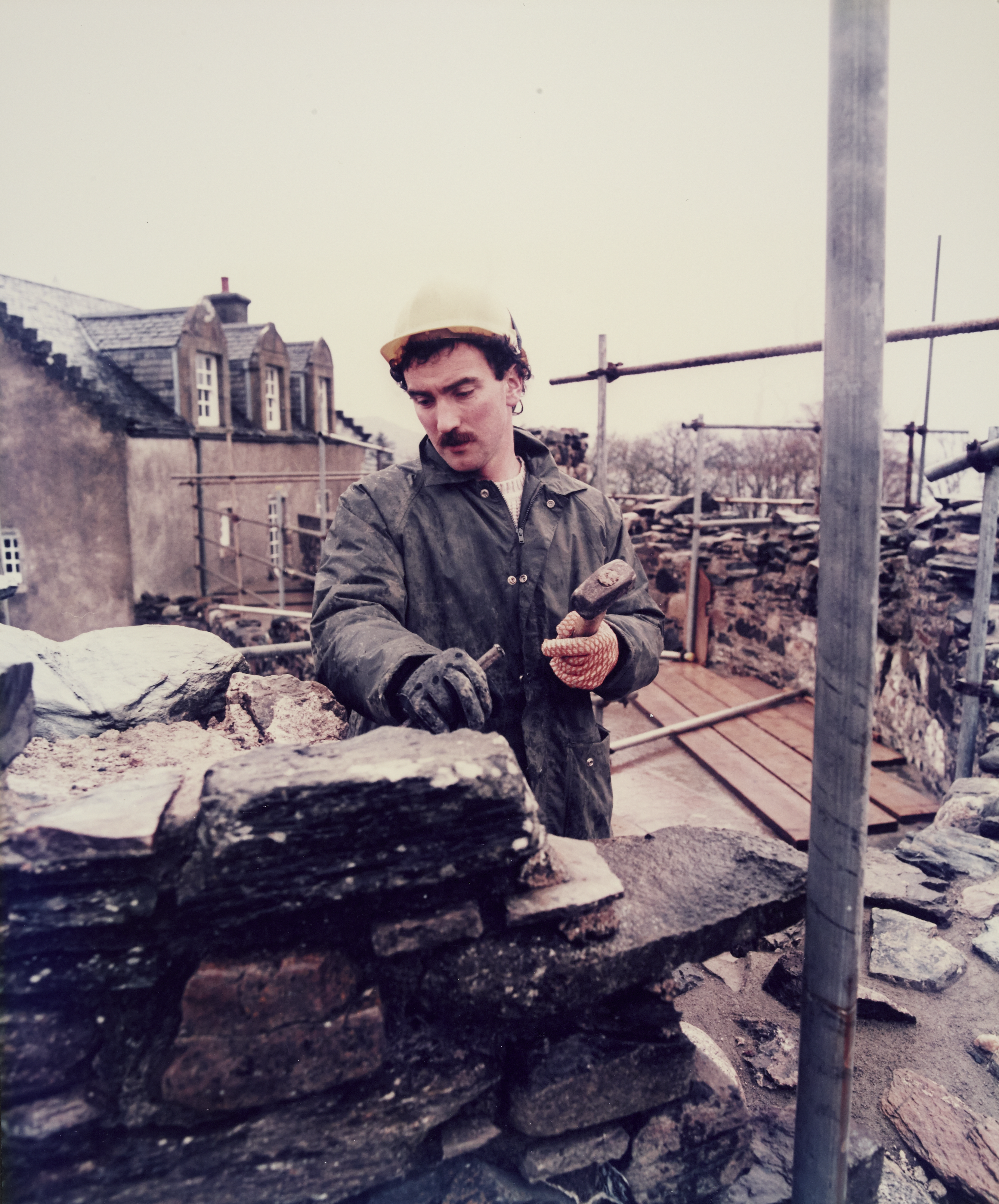 A man in a yellow safety hat and overalls works on a section of a wall