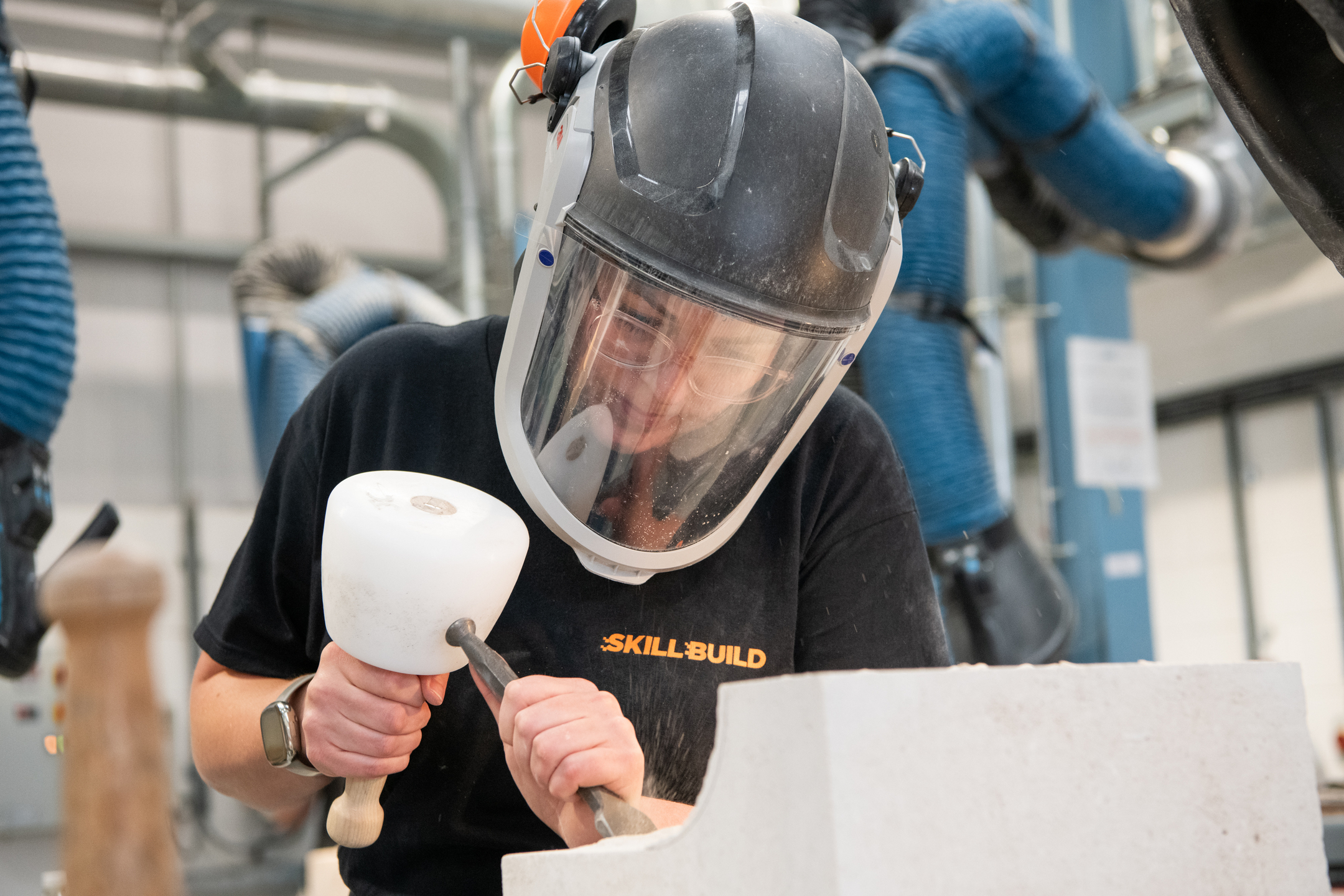 A stonemason wearing protective headgear works on a piece