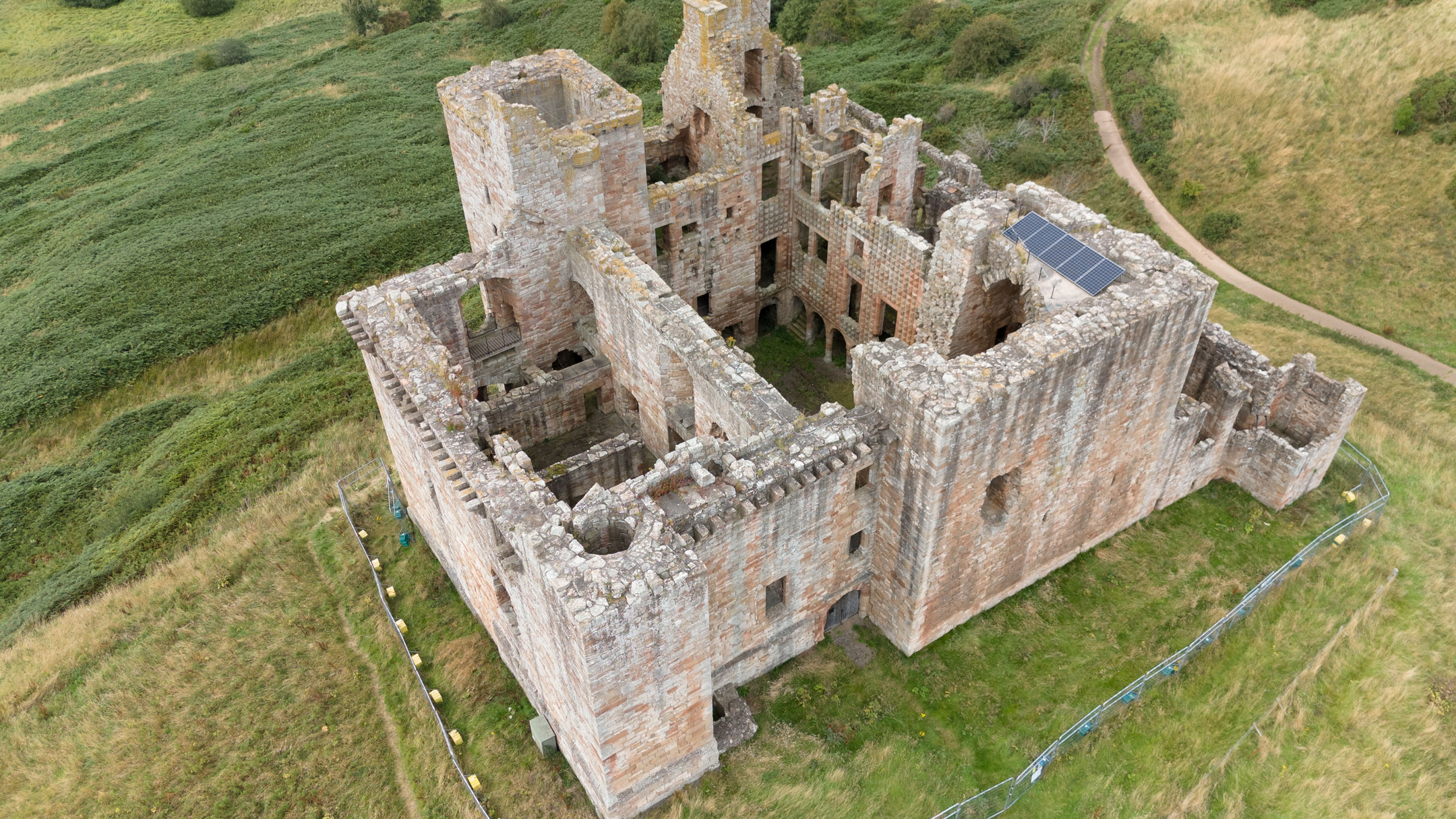 Aerial view of Crichton Castle behind some fencing