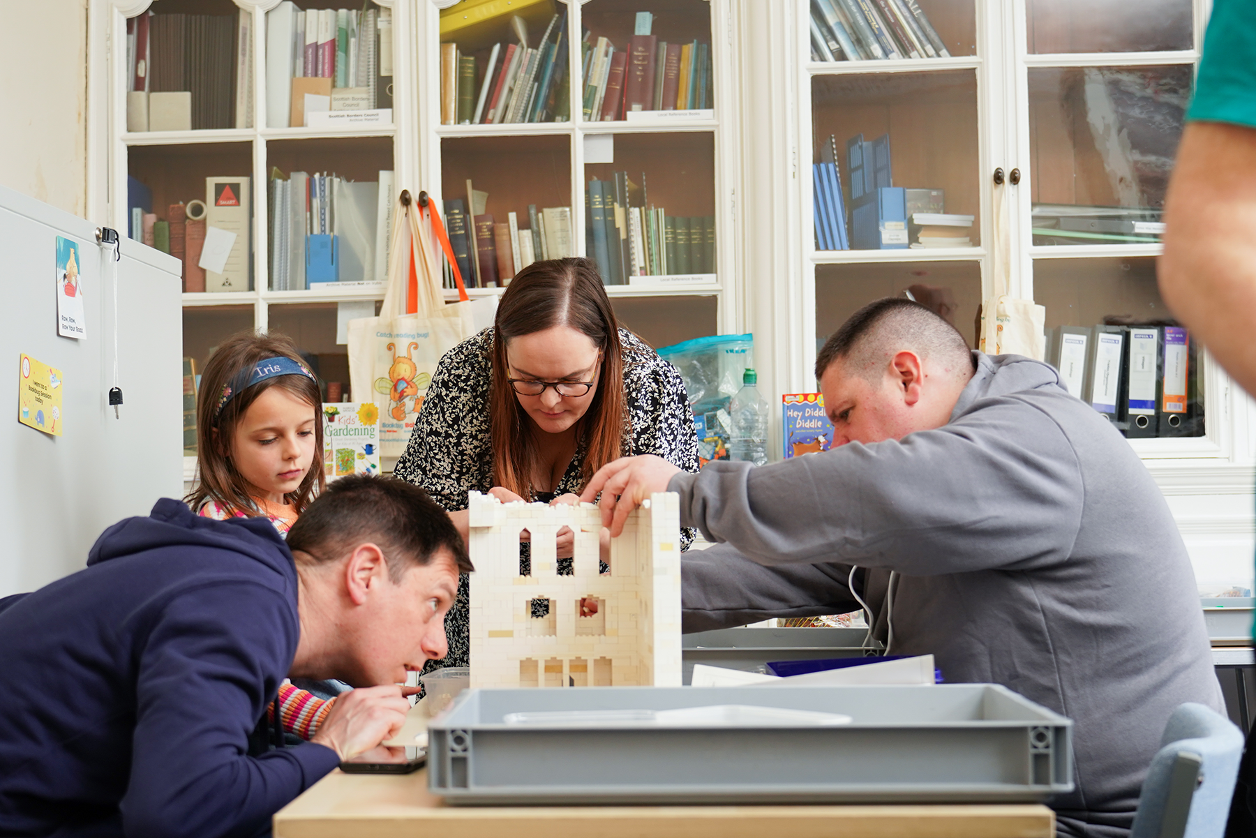 A child and three adults sit around a table building a LEGO castle together