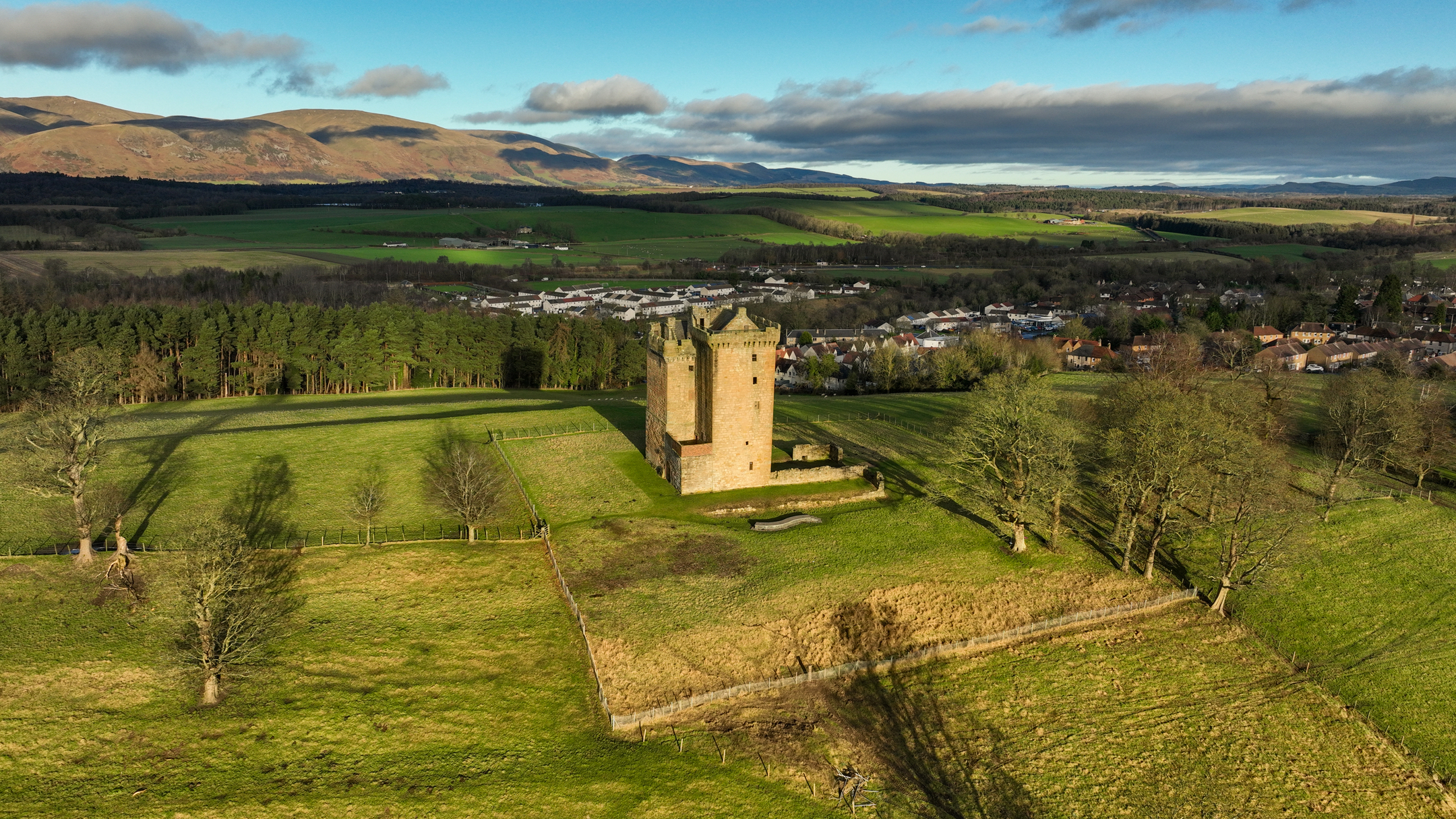 Aerial view of countryside with hills in the distance, a town in the middle and a tower just in front of it