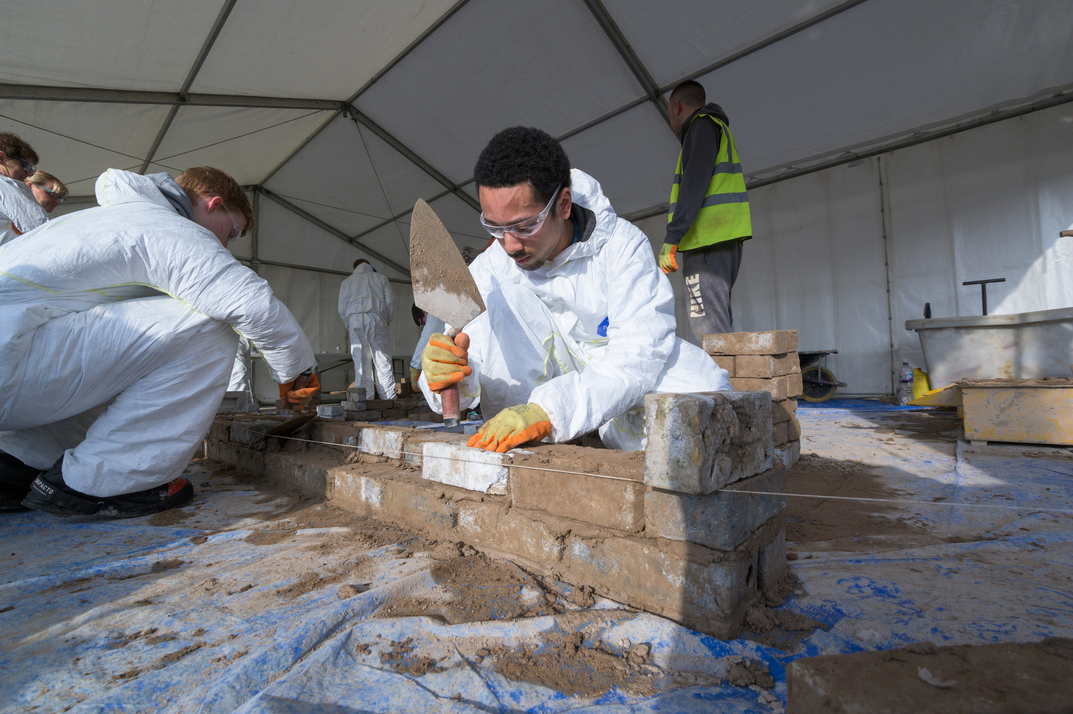 Tow young college students try bricklaying inside a gazebo.
