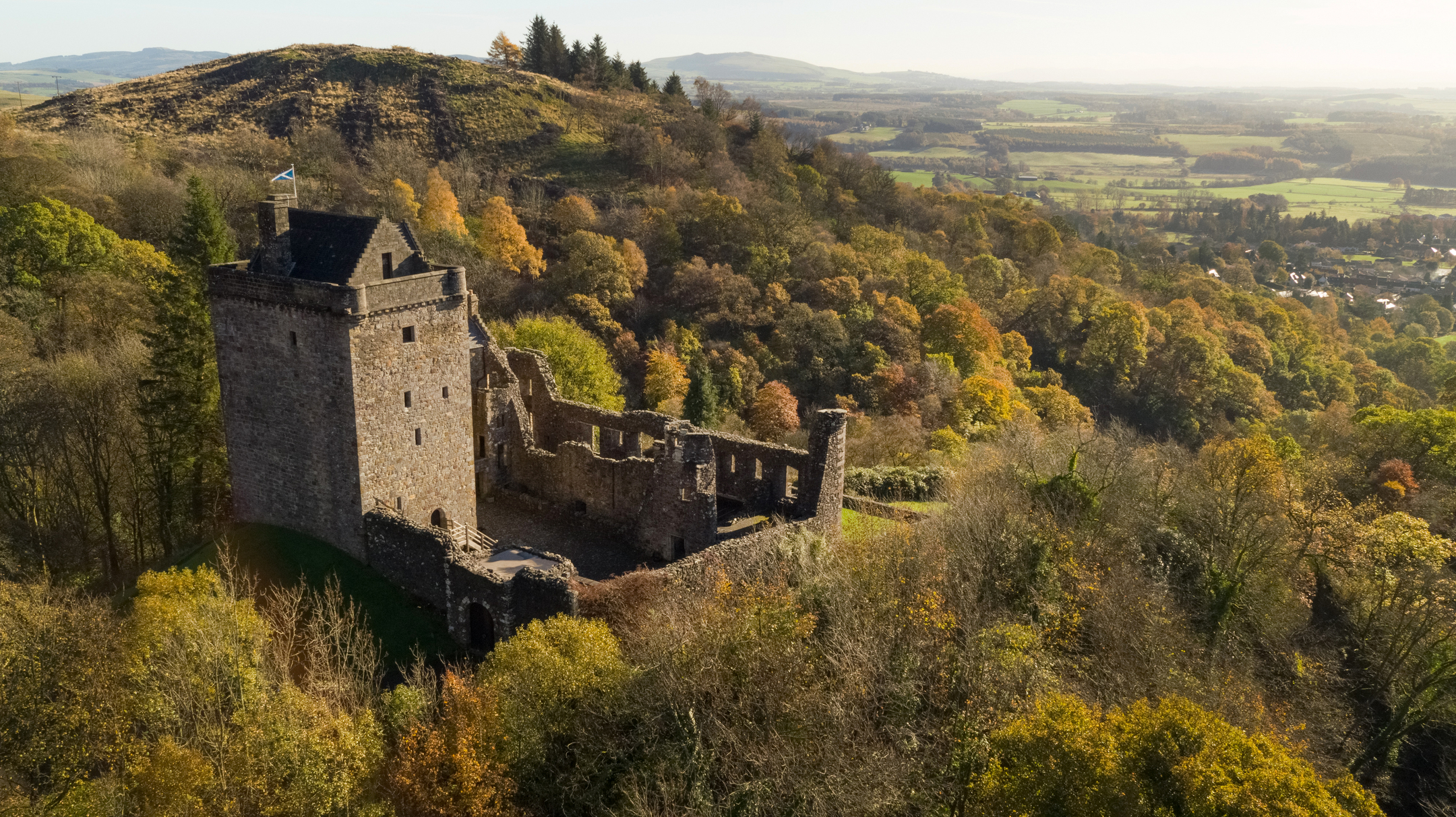 Angled view of Castle Campbell amongst trees changing to autumn colours. 