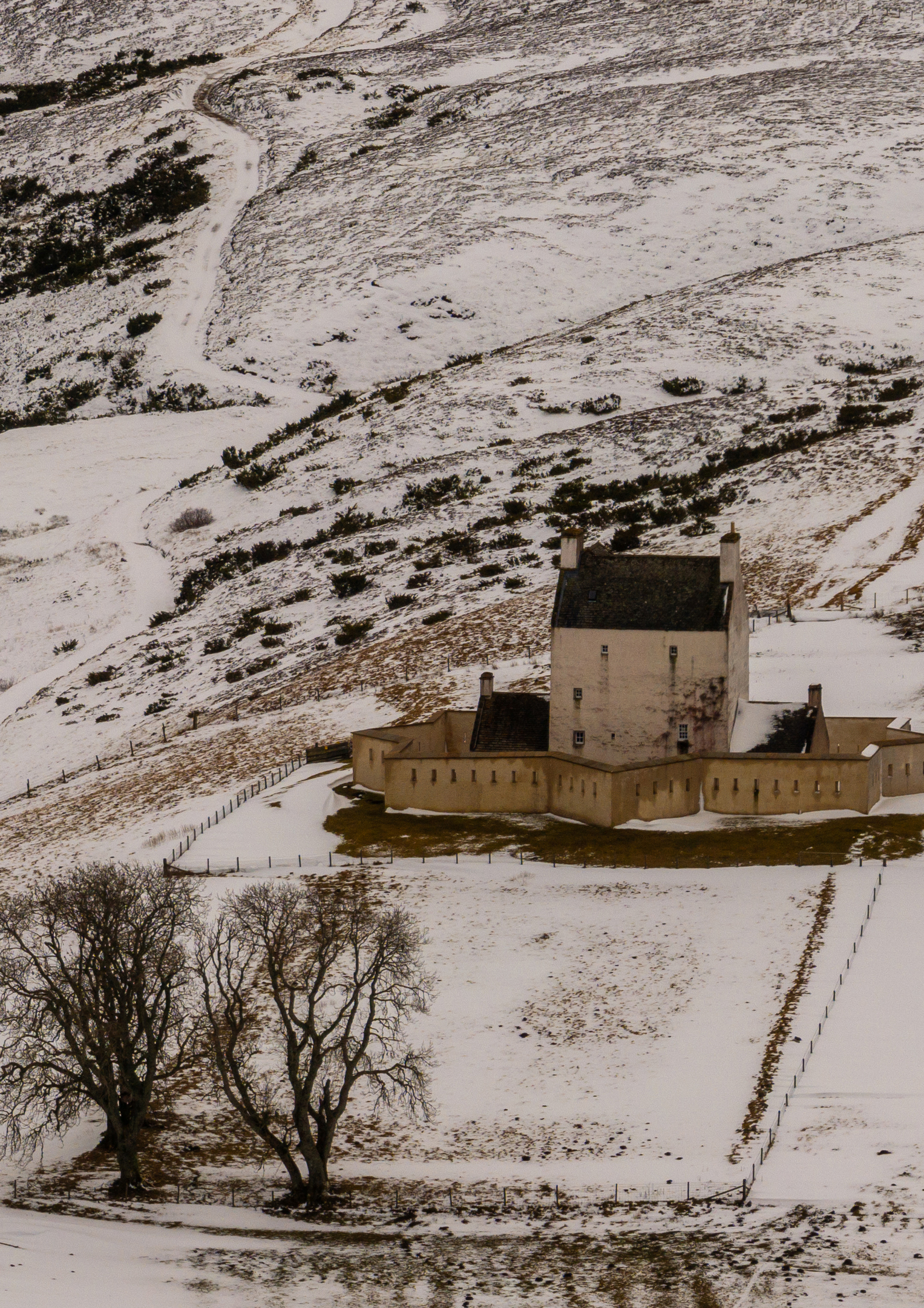 Corgarff Castle in a winter landscape, the white tower and star-shaped wall contrasting with snow-covered hills nearby.
