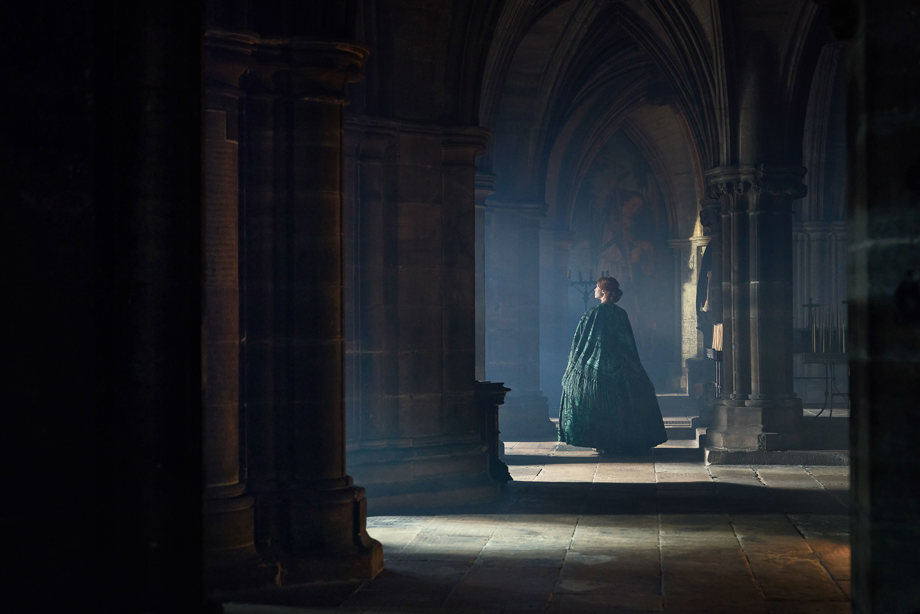 A woman in a long green cape walking through a nave