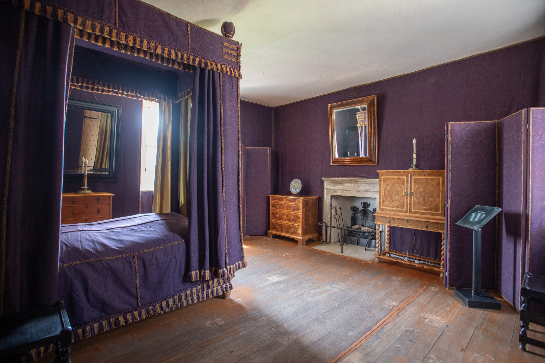 A bedroom in a lavish historic townhouse. A four poster bed is surrounded by purple curtains with a gold trim.