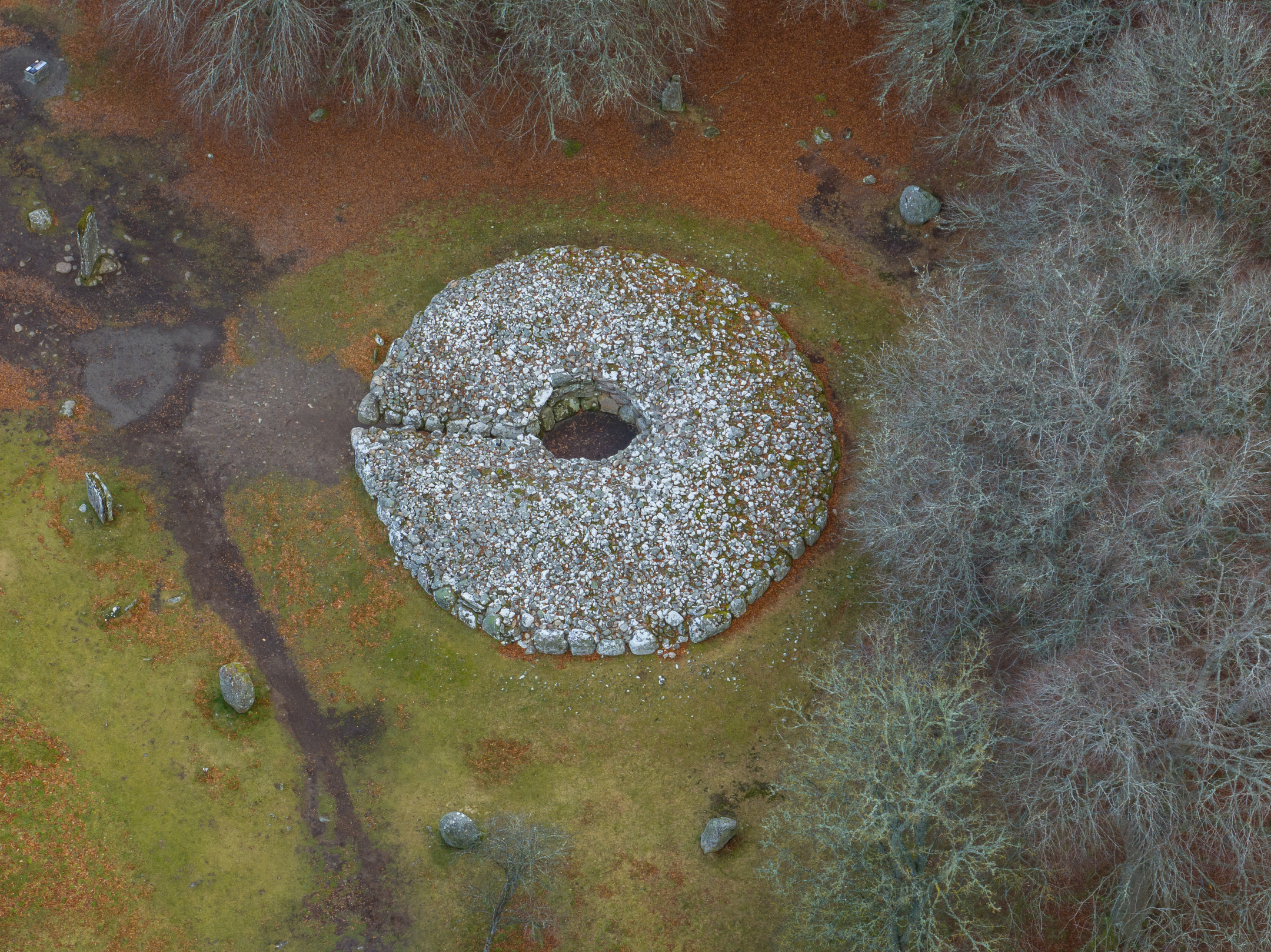 A cairn made from grey stones from above, surrounded an unusually-coloured autumnal landscape