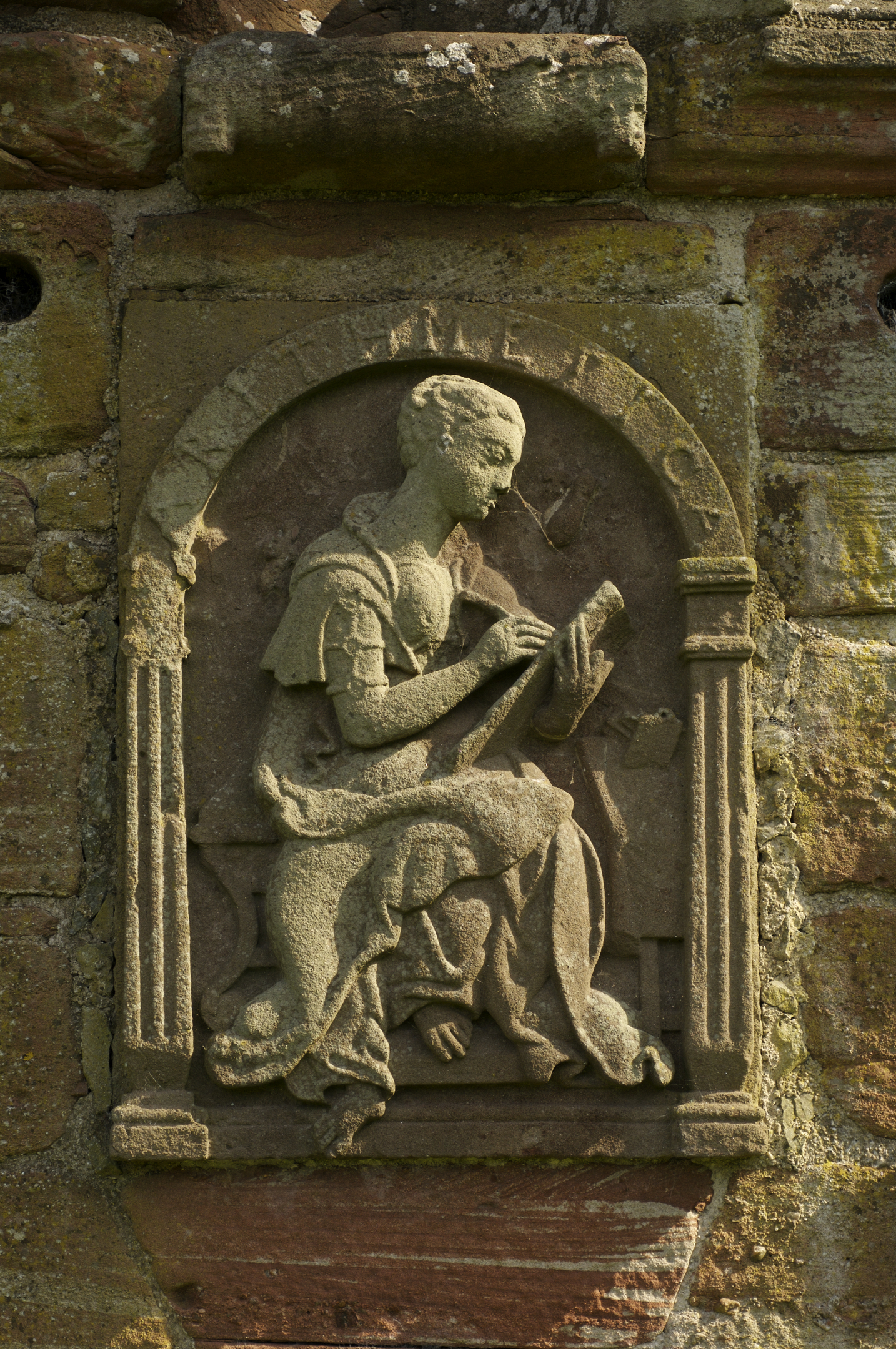 An intricately carved stone panel on the garden wall at Edzell Castle. It depicts a classical figure writing onto a parchment or a tablet. 