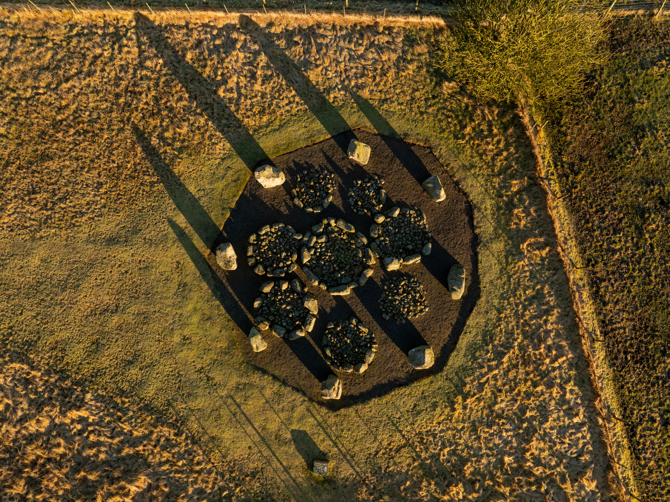 Direct overhead aerial view of the stone circle, clearly showing the ring of standing stones and the eight cairns arranged in a symmetrical pattern inside.