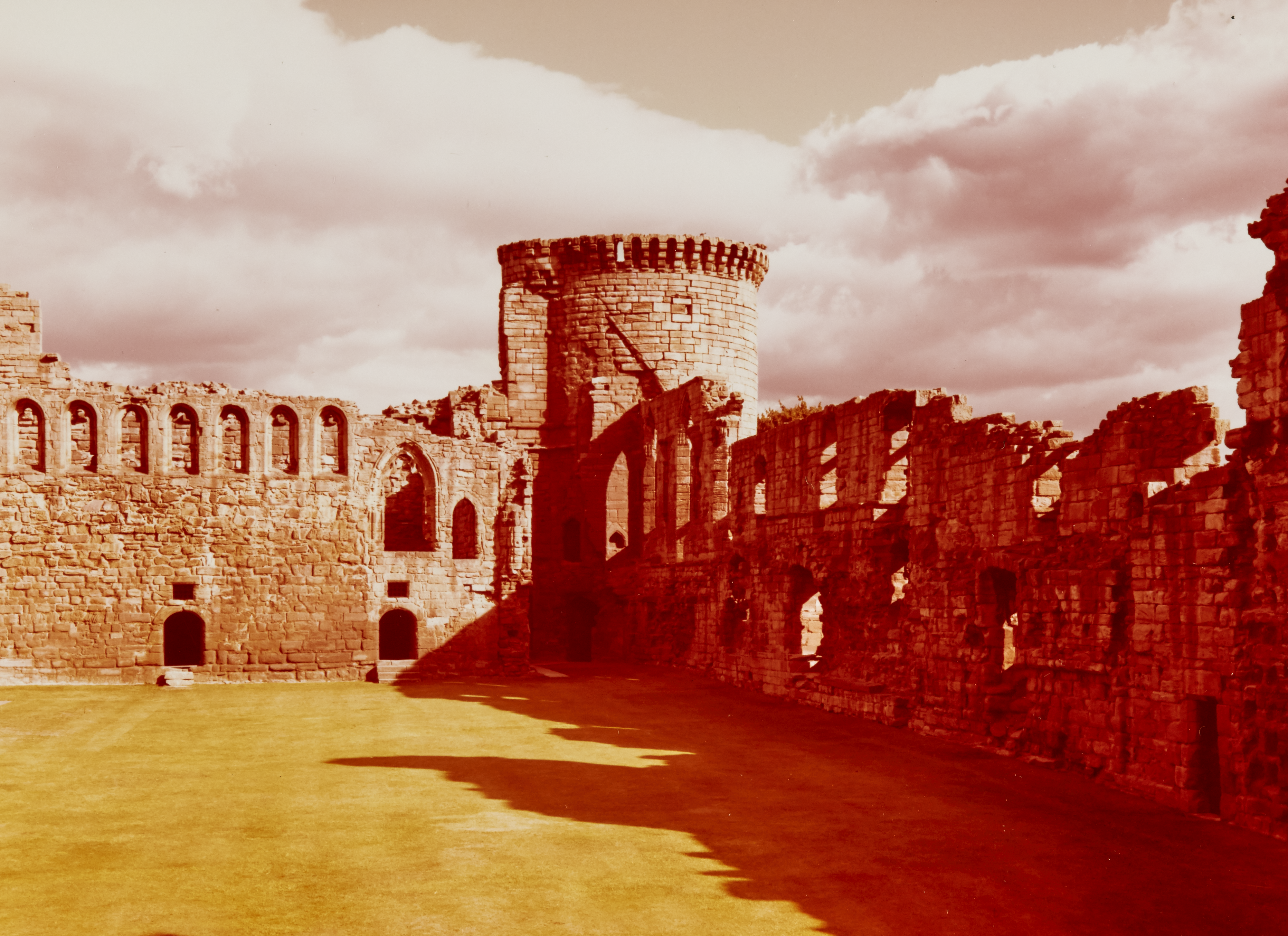 Warm toned photo taken inside Bothwell Castle ruins with the sun casting heavy shadows from one of the main walls