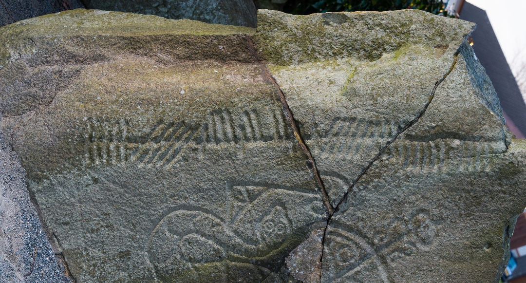 A large stone broken into segments, with visible carvings on the surface.