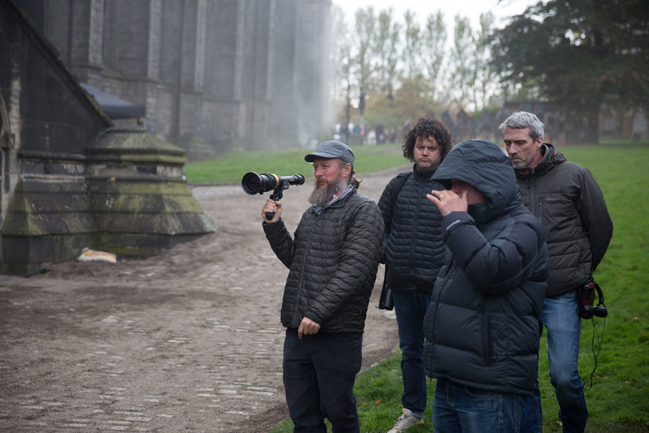 Four members of a filming crew in the grounds of a historic building in the rain and fog