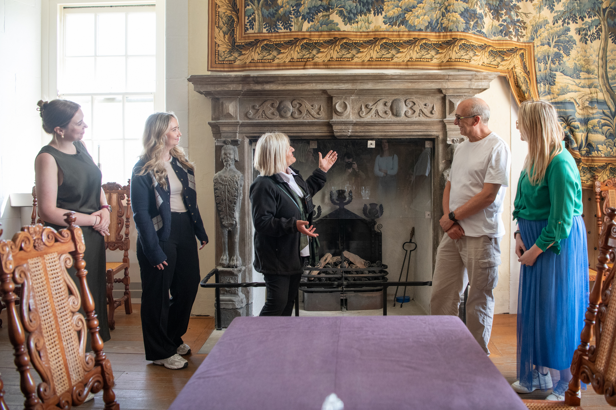 A tour guide shows visitors to a historic townhouse an ornate stone fireplace.