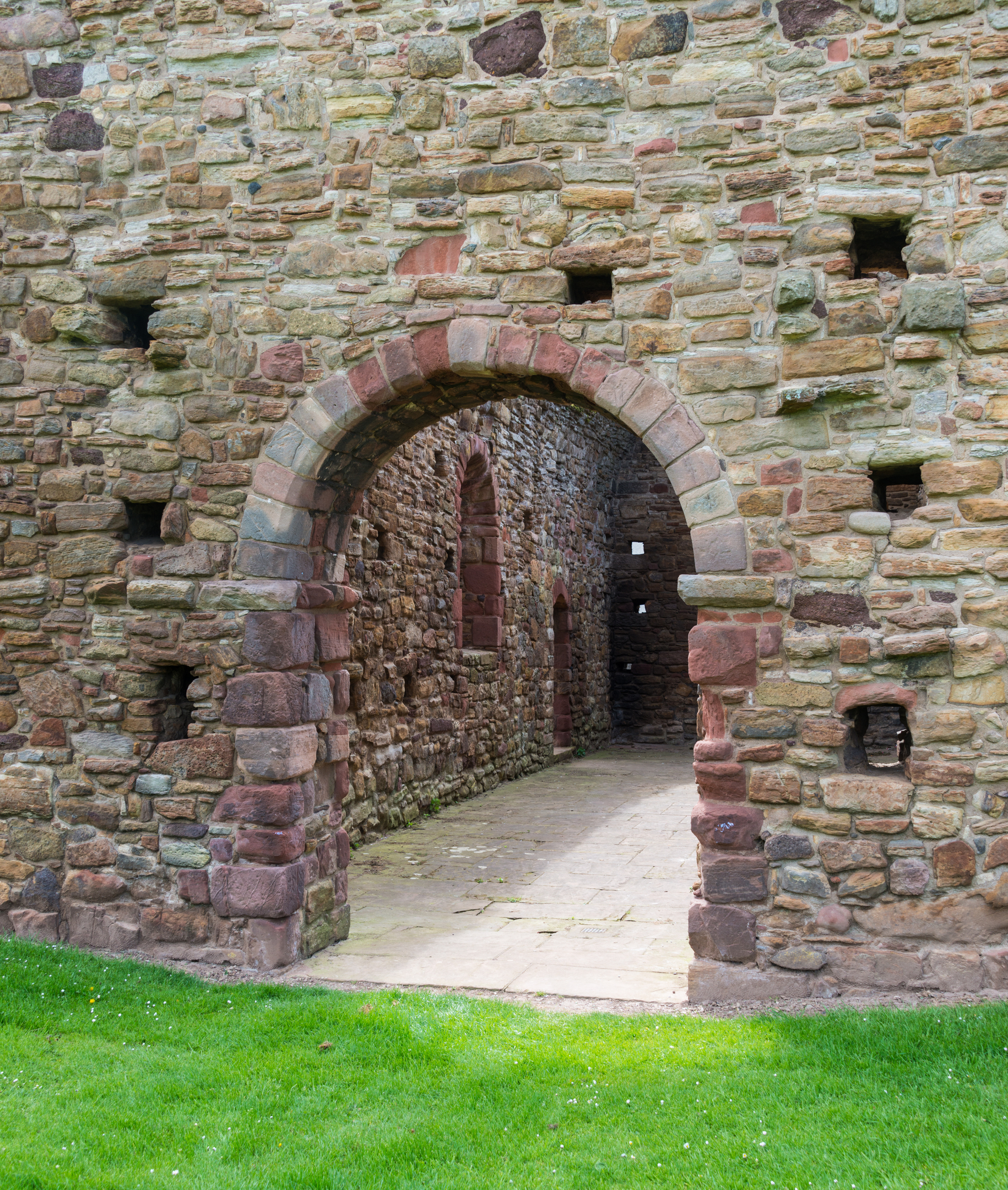 A close-up of a rounded stone archway leading into the interior of the historic ruin, with grass in the foreground.