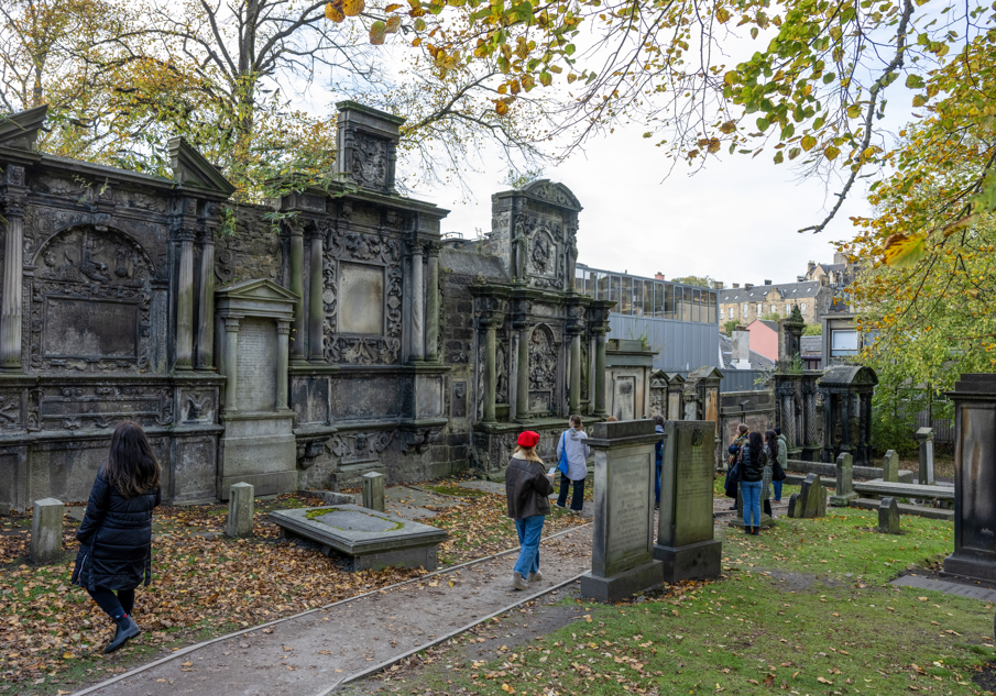 It is an sunny, early autumn day in Edinburgh's Greyfriers Kirkyard Cemetry, and a group of people are walking through the grounds looks at some of the stonework.