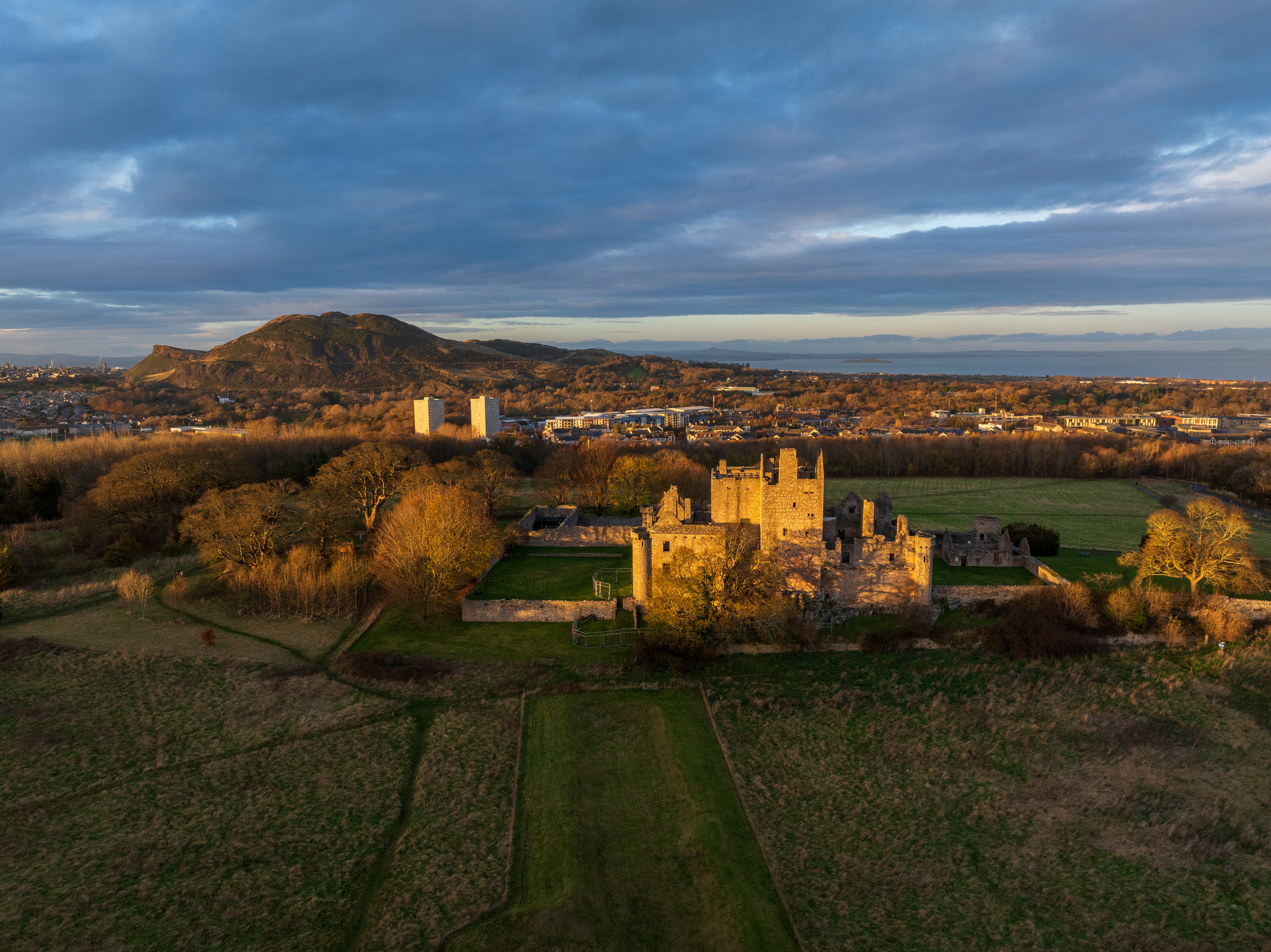 The castle’s stone towers glow in late afternoon light, set against autumn trees and the city skyline.