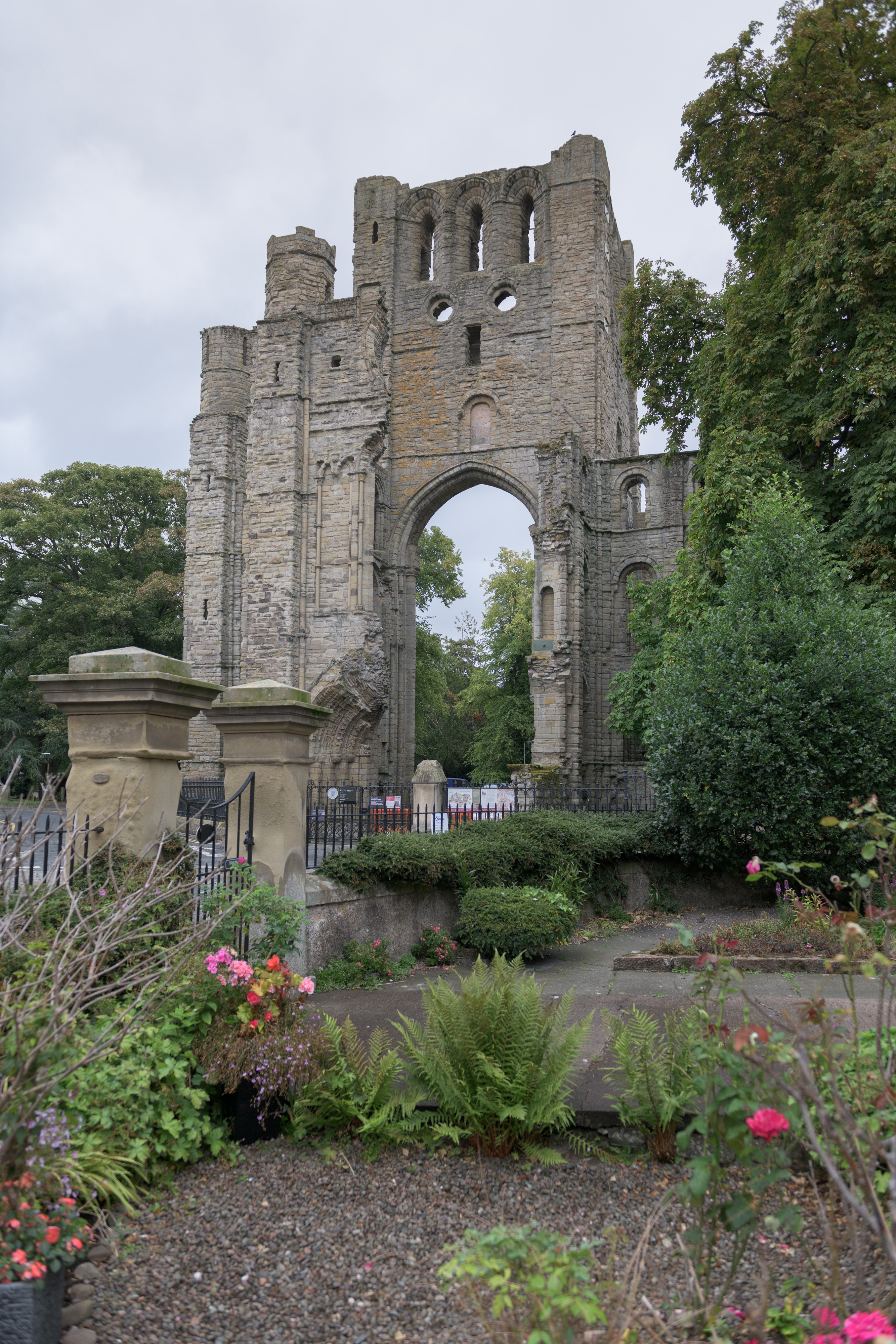A large, stone abbey ruin, with pink flowers planted in the ground in front of it