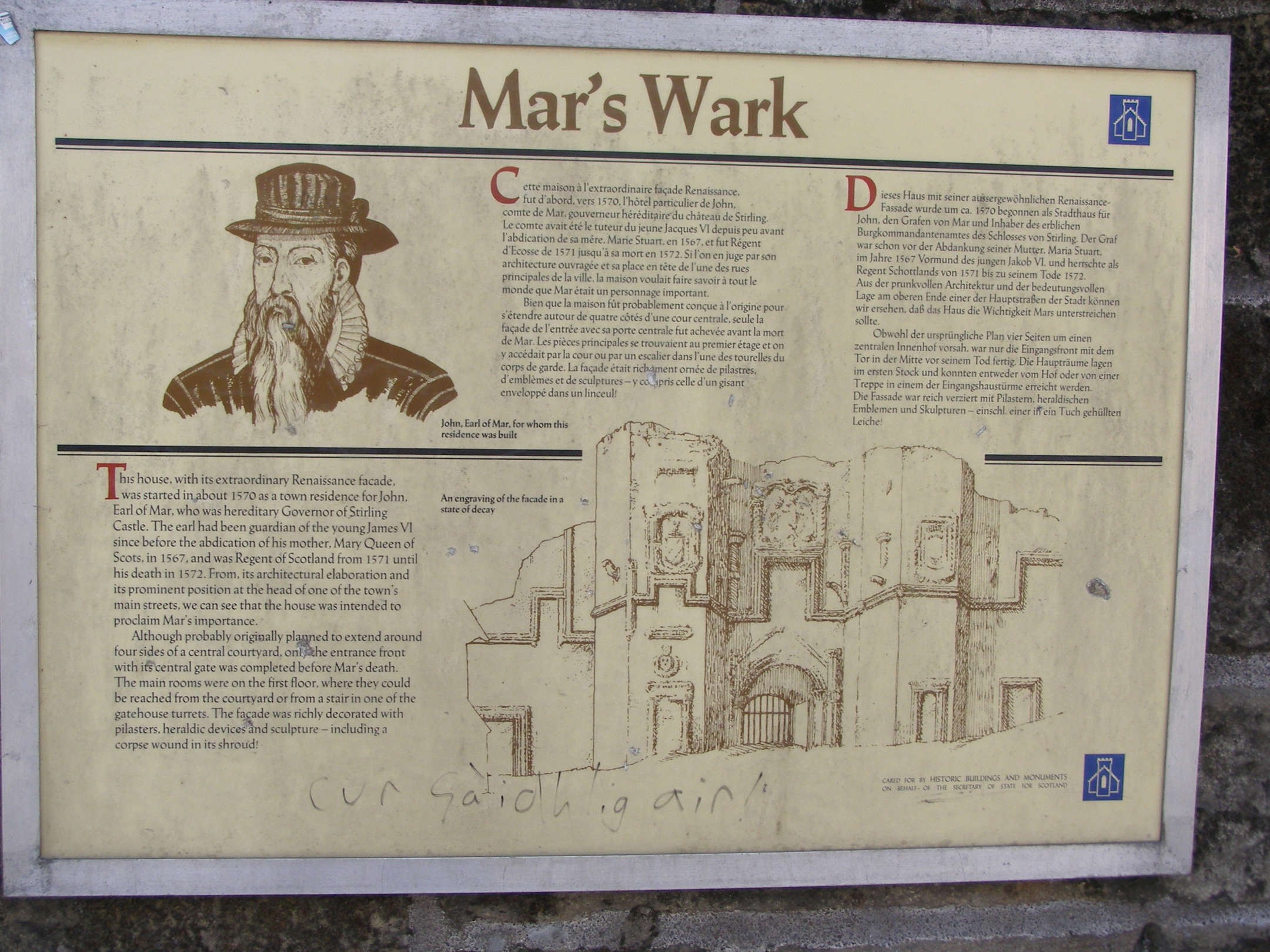 Interpretive panel titled ‘Mar’s Wark’ mounted on a stone wall. The sign contains historical text about the building’s origin and architecture, along with an illustration of the original facade showing symmetrical towers and decorative details. The panel includes a stylized portrait and explanatory sections about the structure’s significance.