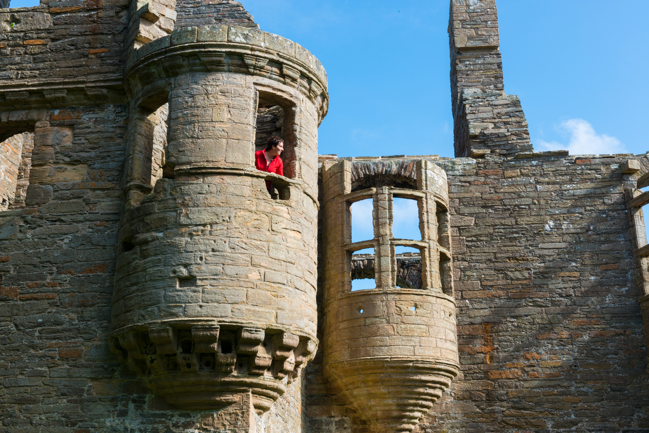 A person standing inside a small rounded tower window of a palace ruin, looking outward toward the courtyard below.