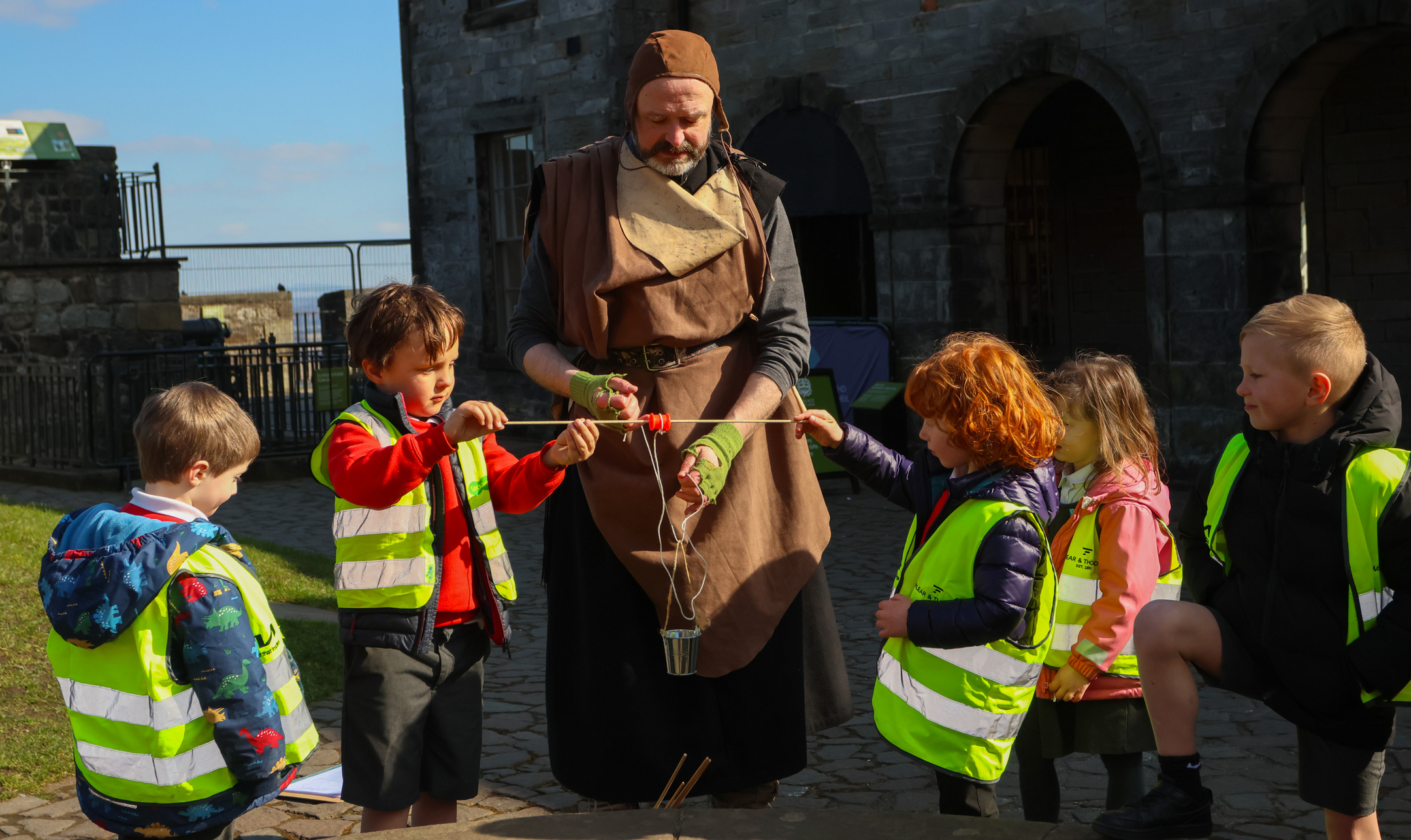 Pupils in high vis jackets interact with a costumed interpreter outside at Stirling Castle