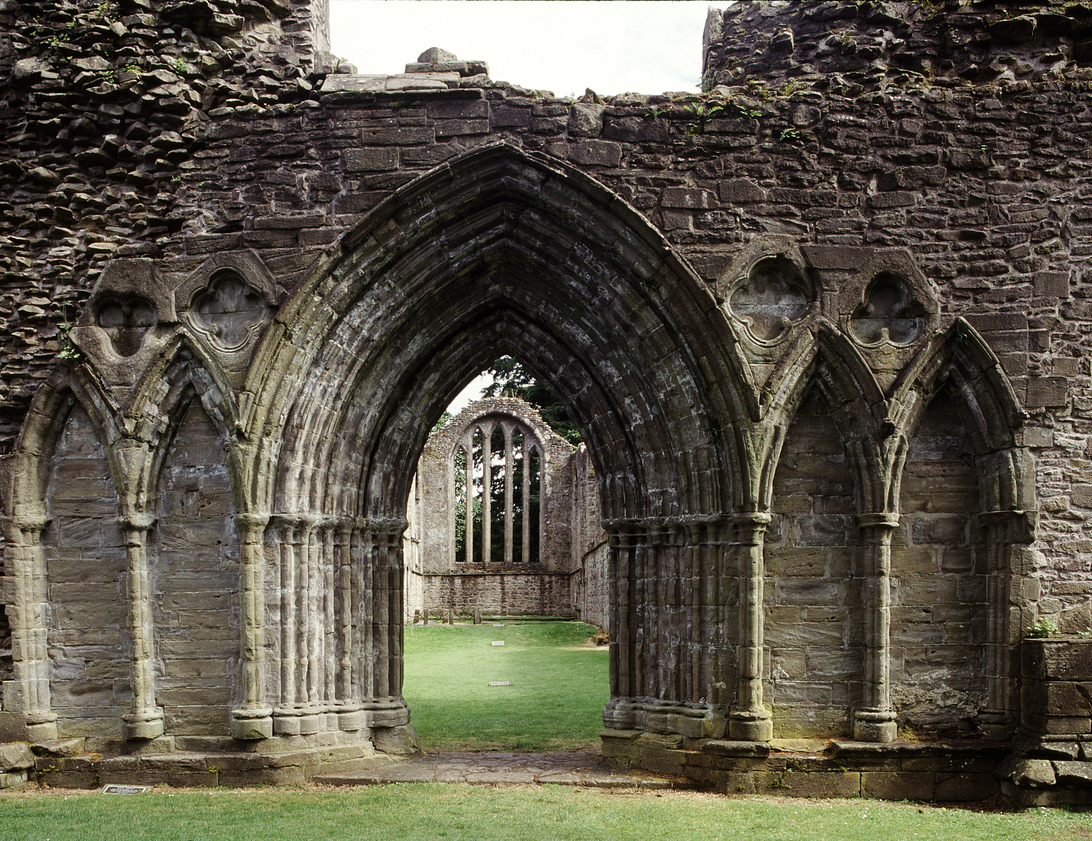 A close-up of an ornate Gothic stone archway framing a view of a large and ornate window.