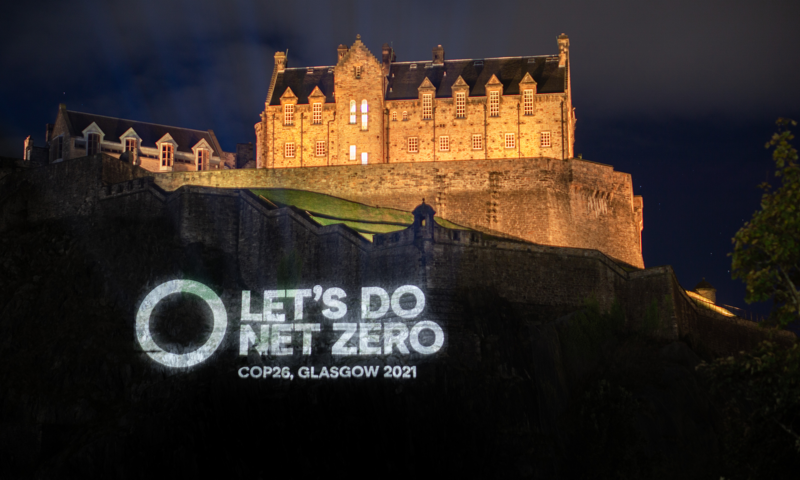 A circle outline beside the text "Let's do net zero. COP26, Glasgow 2021" is projected onto the cliffs below Edinburgh Castle at night.