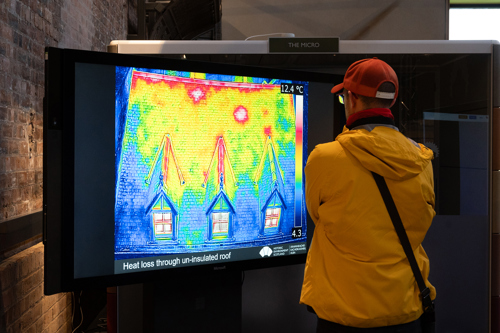 A person looking at a tv screen seeing heat maps showing heat loss through an un-insulated roof