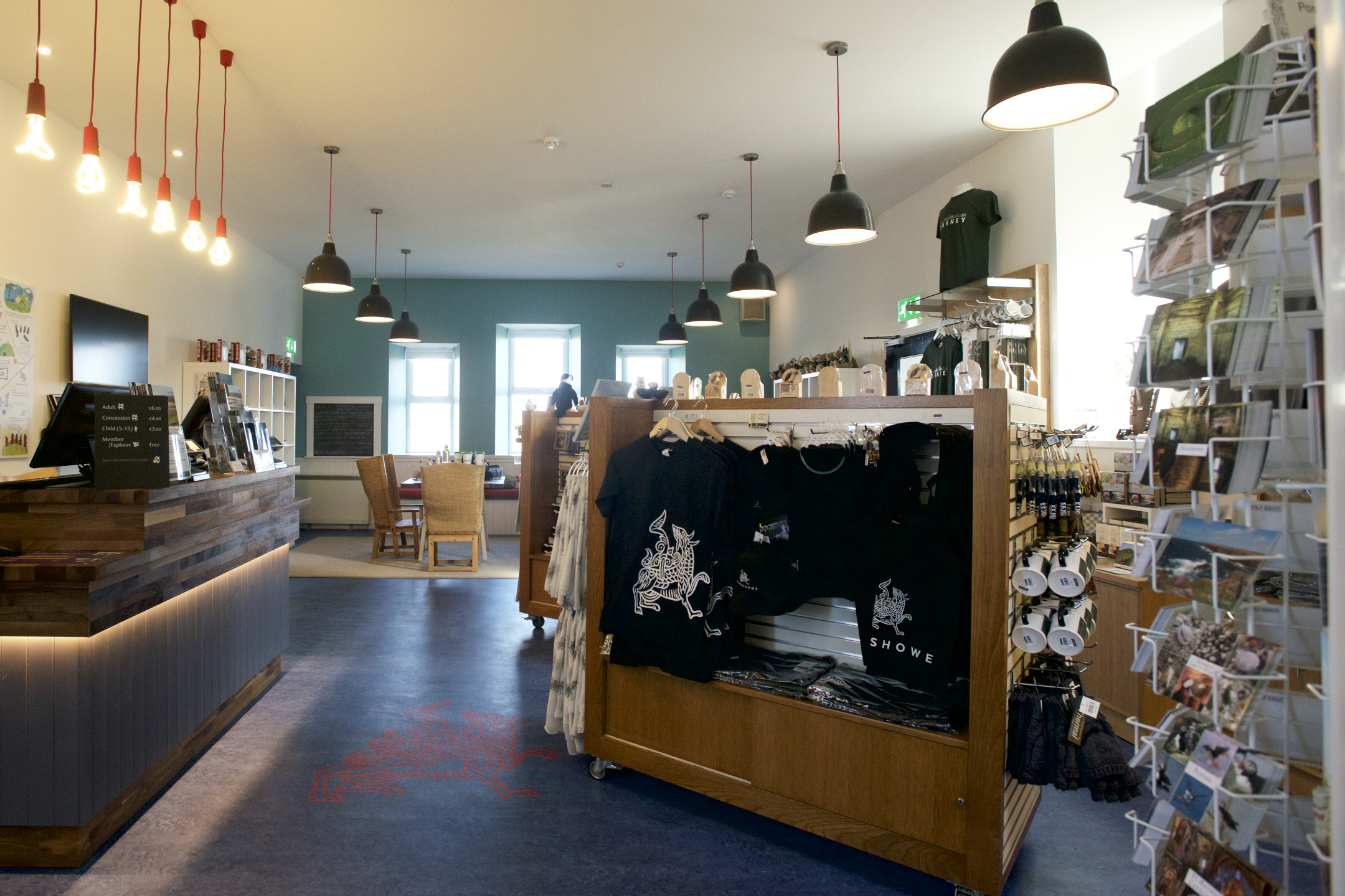 Gift shop with stand with items featuring the Maeshowe dragon and a postcards stand.