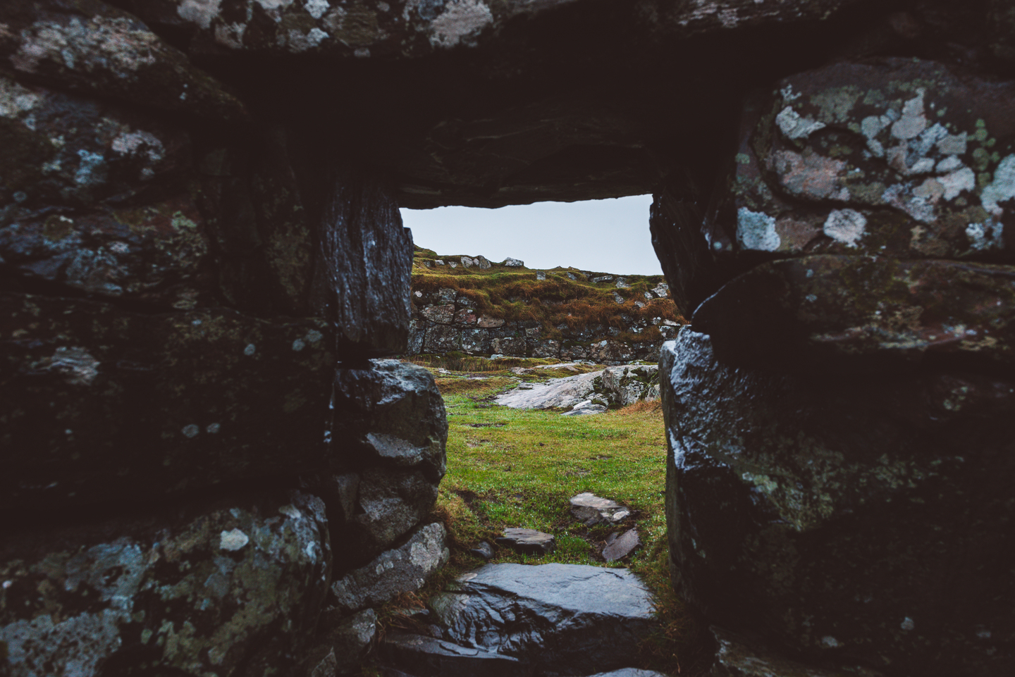 A stone wall with a space in the middle, where you can see sky and grass on the other side.